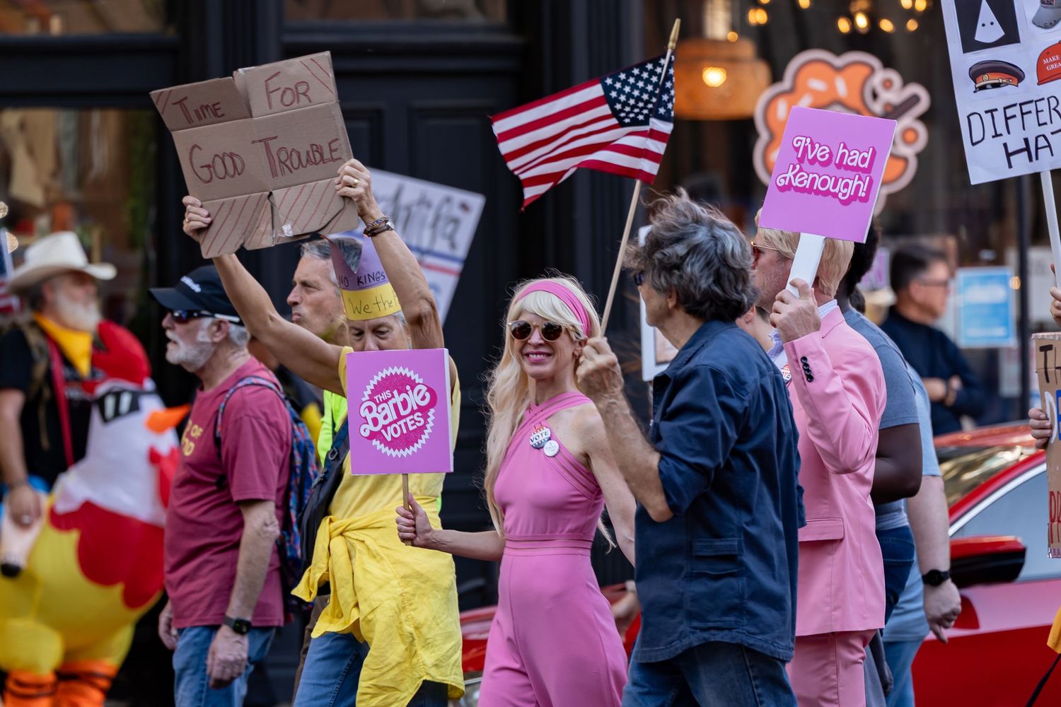 Protesters holding colorful signs gather outside a building during a demonstration.