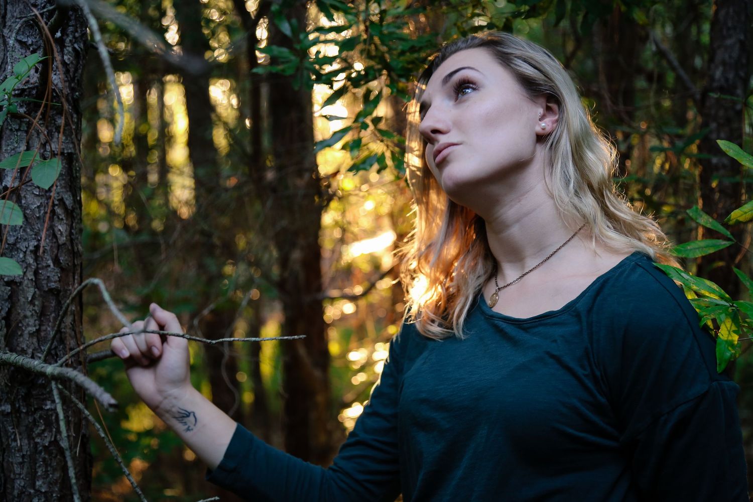 Individual posing thoughtfully against natural forest backdrop during golden hour.