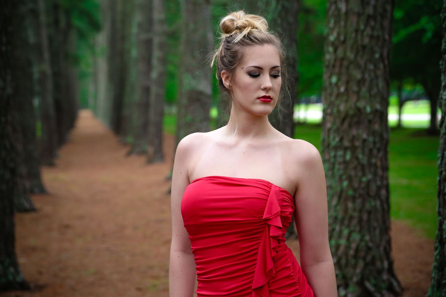 Fashion shoot in a pine forest with red dress creating dramatic contrast.