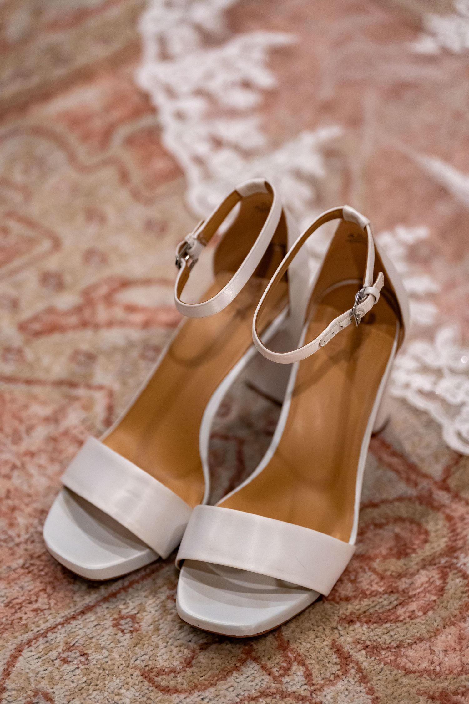 White platform sandals with ankle straps displayed on a patterned carpet.