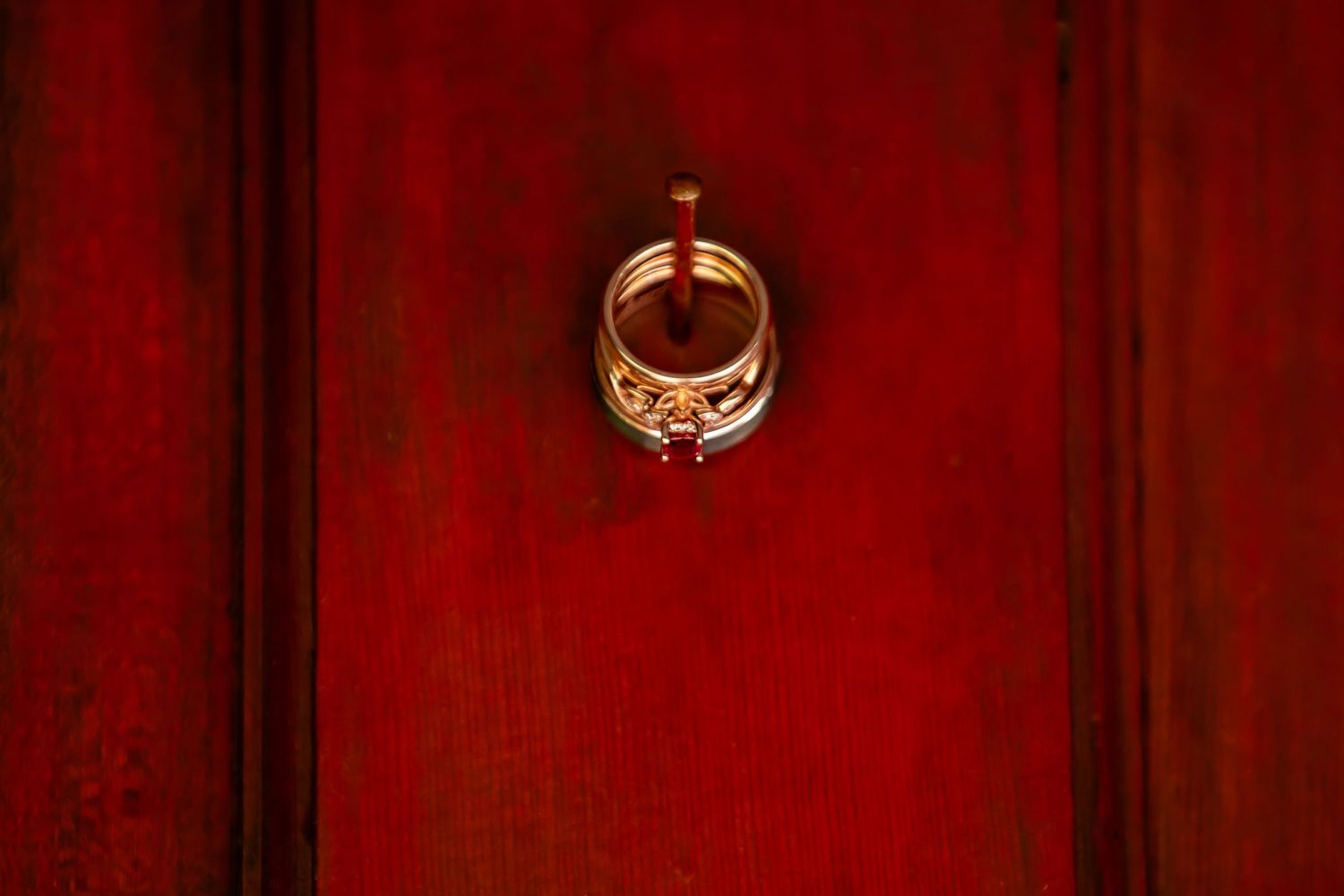A golden wedding ring photographed against a rich red wooden background.