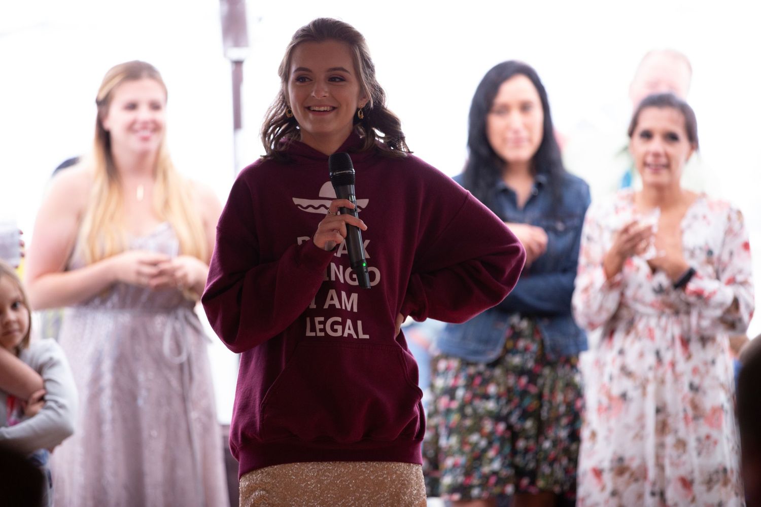 Guest wearing a burgundy hoodie speaks during reception while others watch.