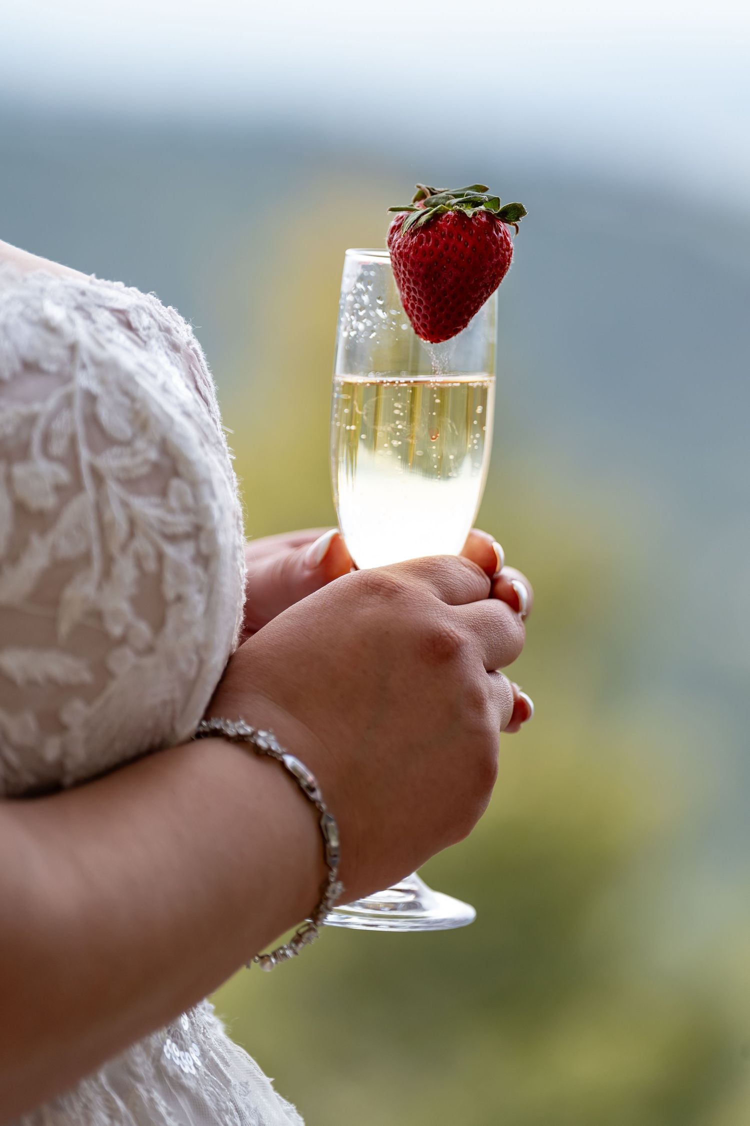 Elegant champagne glass with strawberry garnish held by someone in a white lace wedding dress.