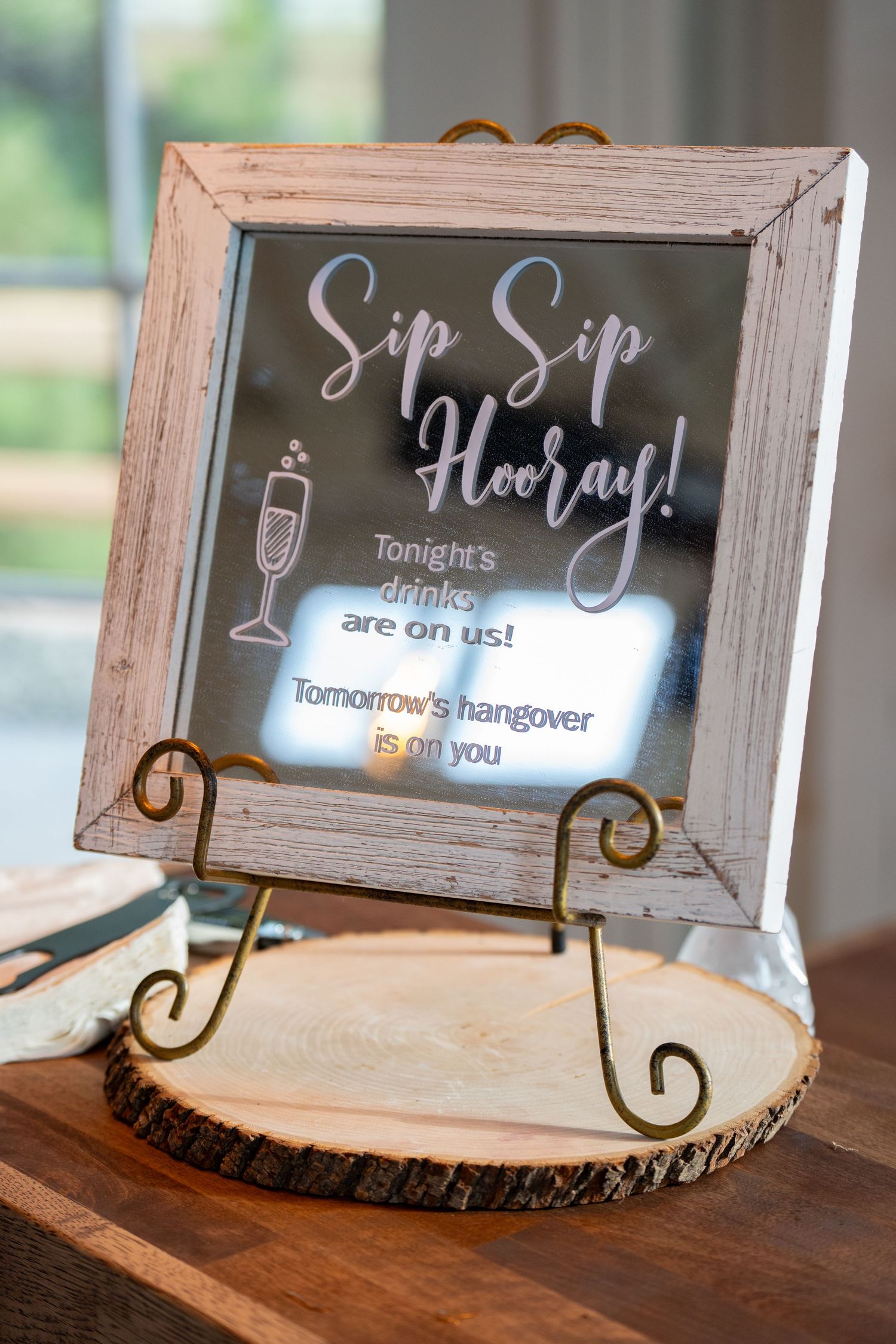 Rustic framed bar sign with humorous quote about drinking displayed on wooden stand.