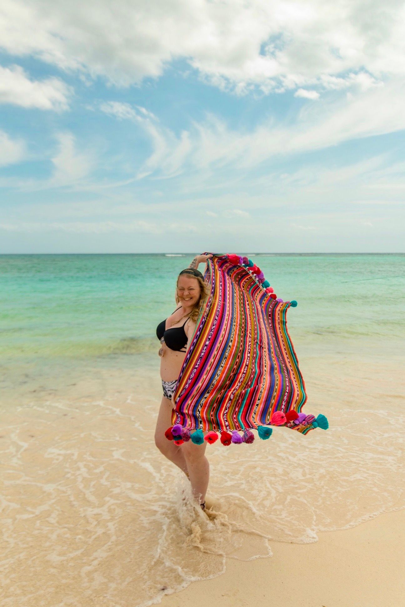 Colorful striped blanket waves in the breeze on a tropical beach with turquoise waters.