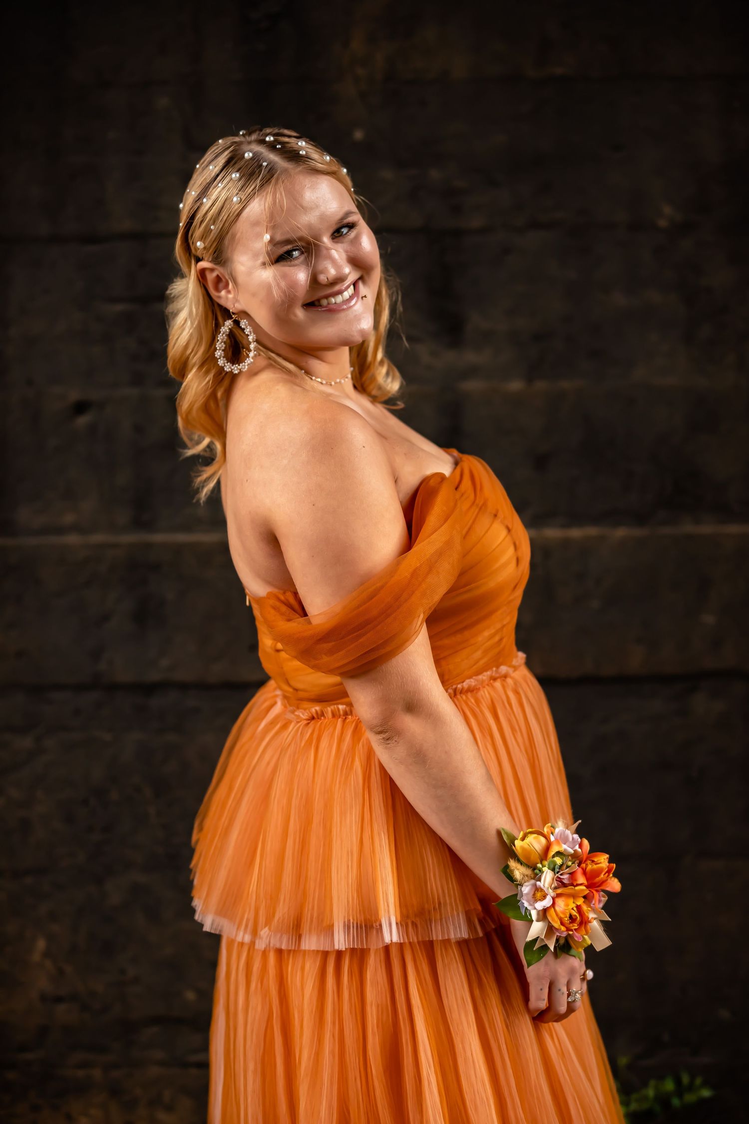 A person in a flowing orange dress poses elegantly against a dark wooden wall.