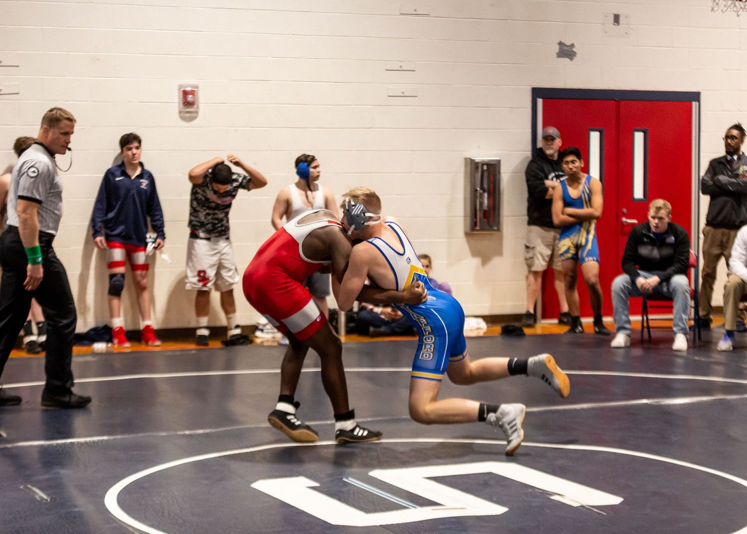 Two wrestlers engaging in a competitive match on a black mat with red borders.