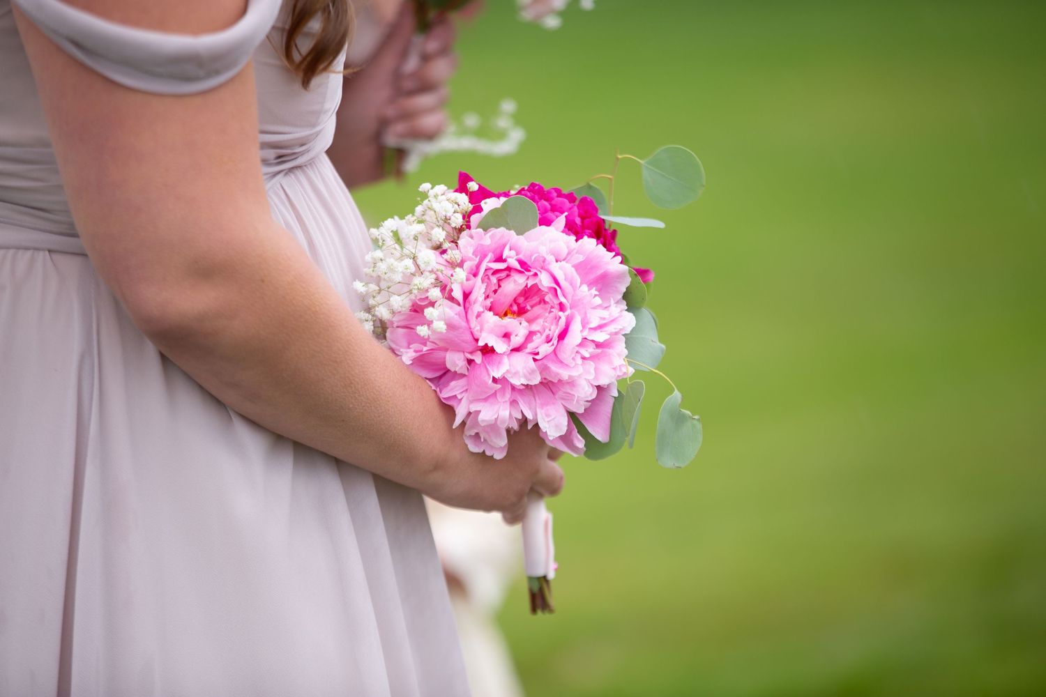 Bridesmaids in light purple dresses hold pink bouquets during an outdoor wedding ceremony.