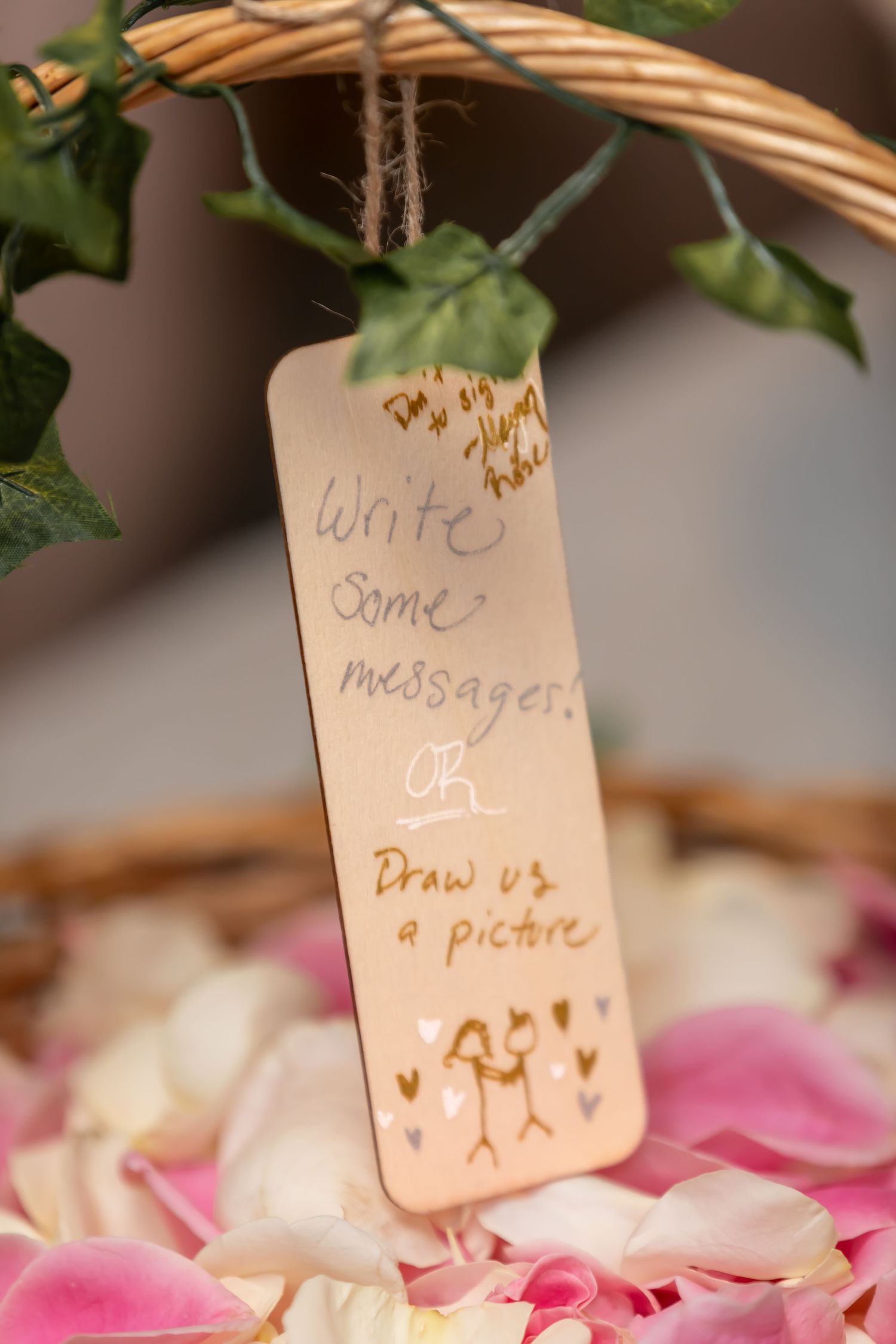 Wedding guest book tags with handwritten messages hanging from twine near pink rose petals.