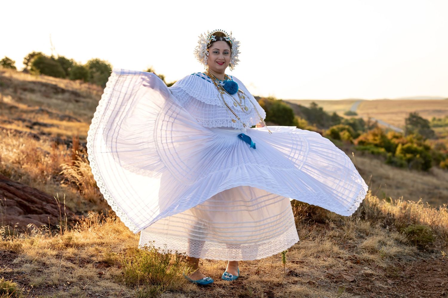 A performer in traditional white dress spins during a golden hour photoshoot in nature.