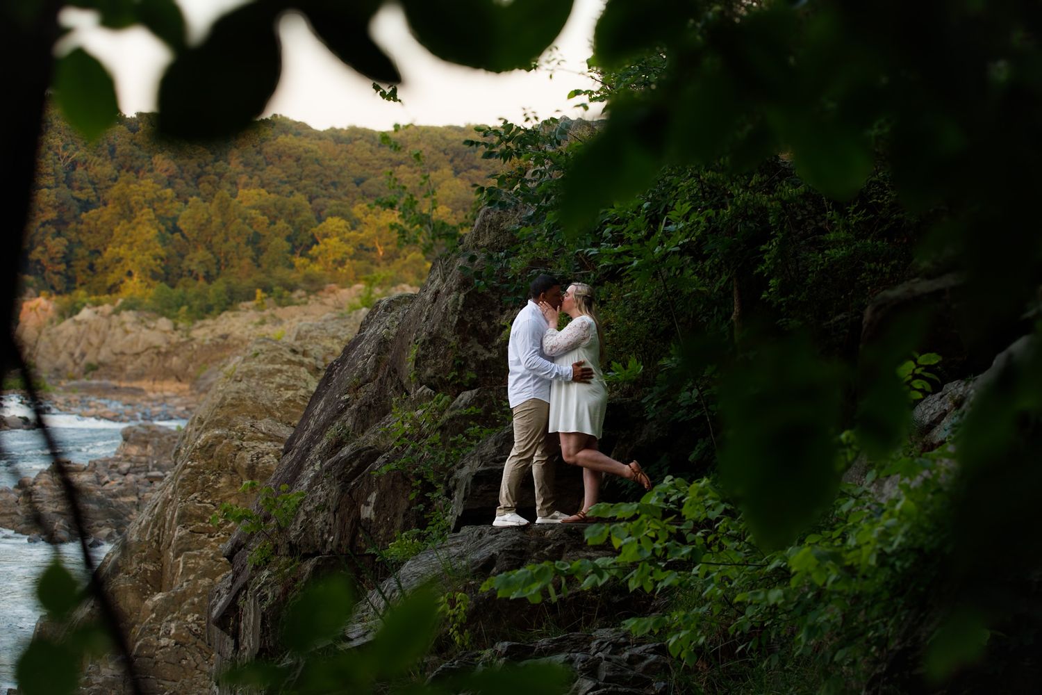 Couple embracing in wooded area with natural lighting.