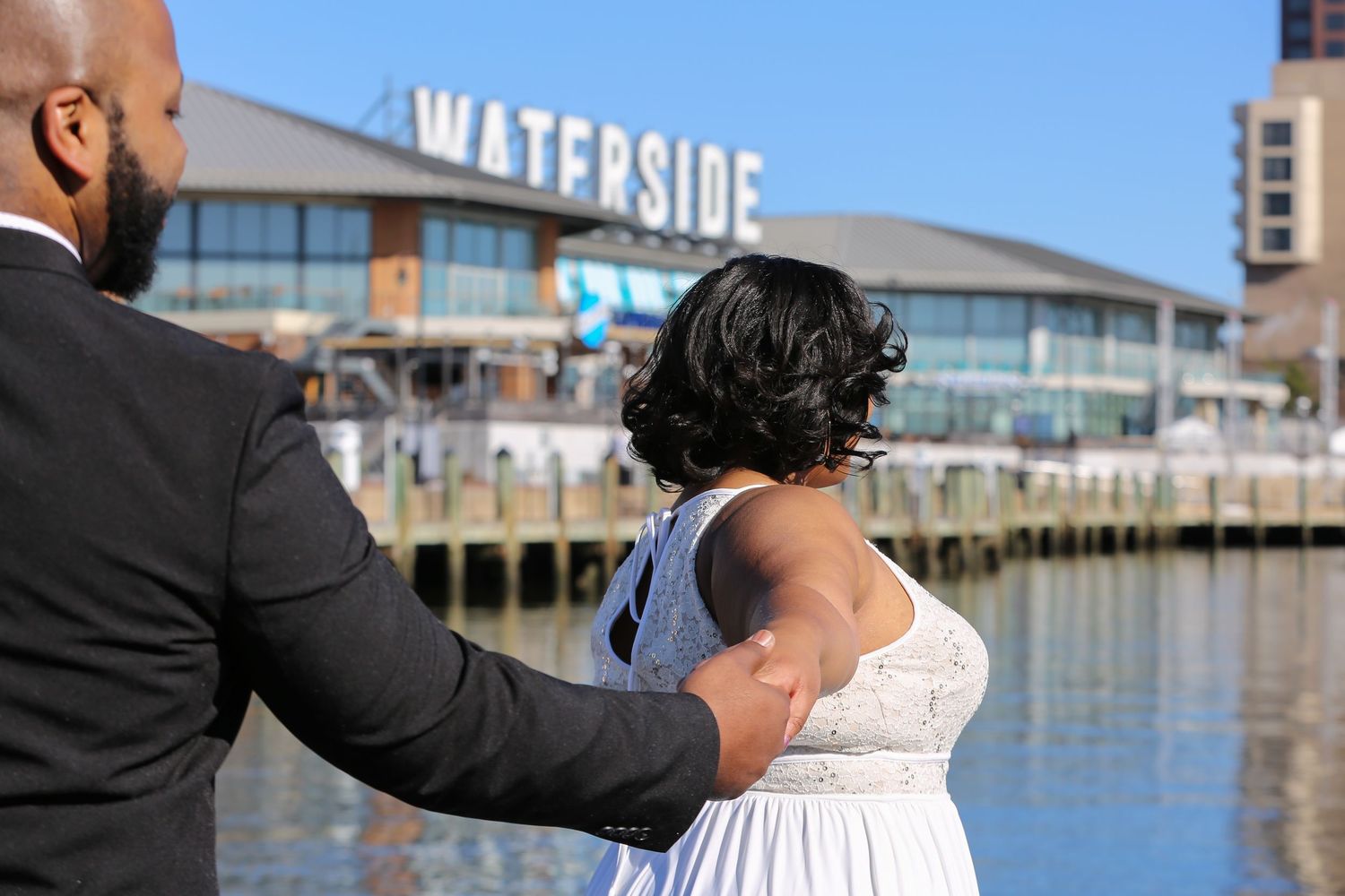Waterfront wedding ceremony with guests seated in white chairs along a dock overlooking a marina.