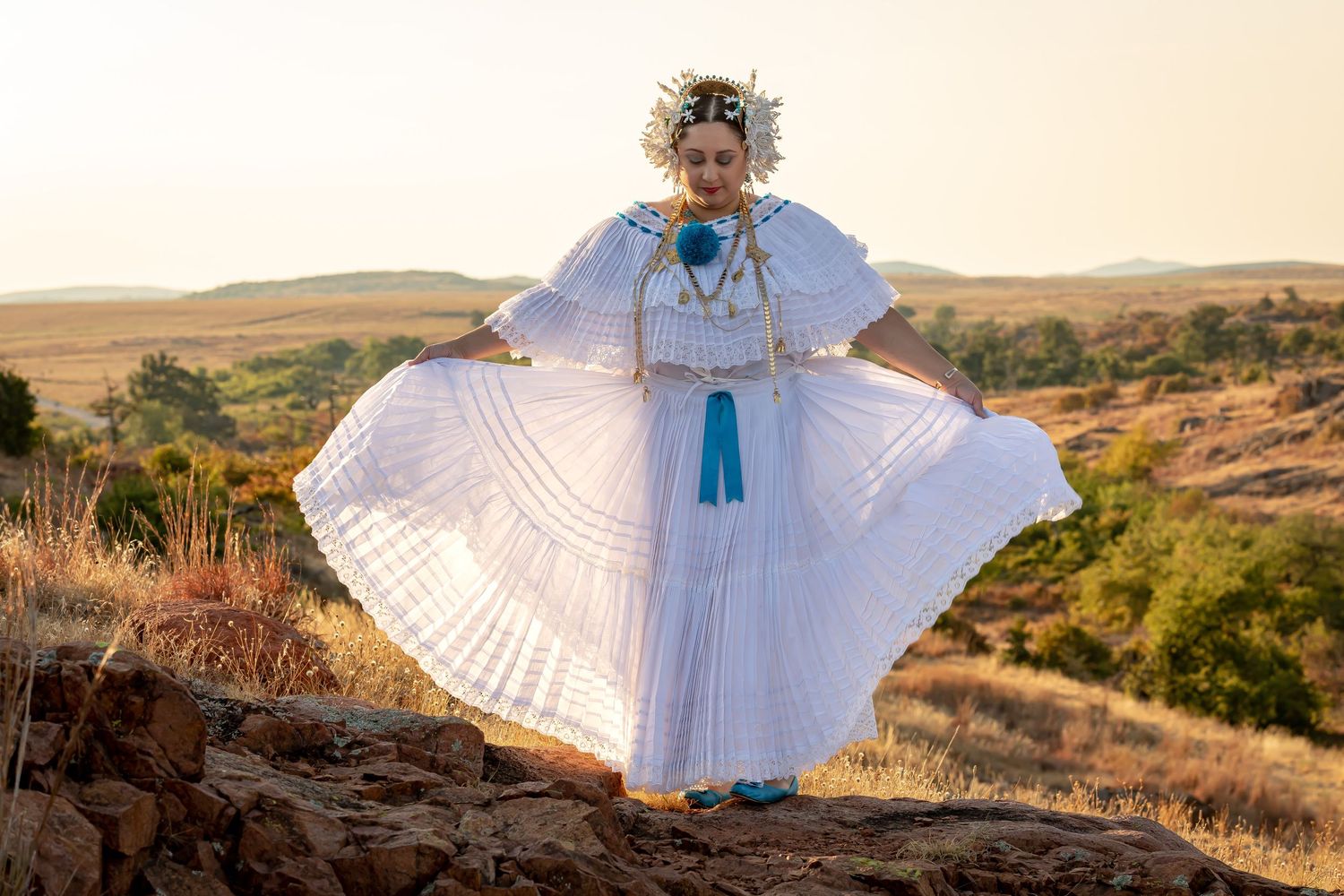 Traditional dancer in white dress and floral crown performs outdoors at sunset.