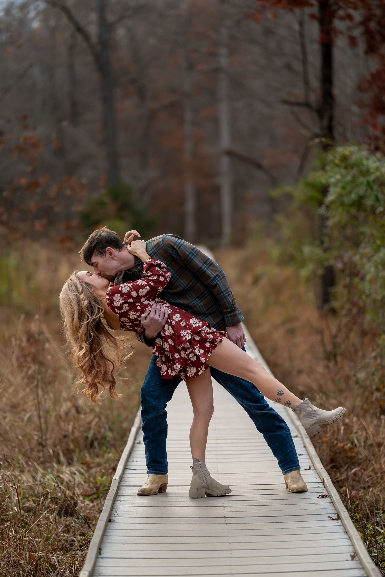 A couple dips dramatically on a wooden boardwalk surrounded by autumn foliage.