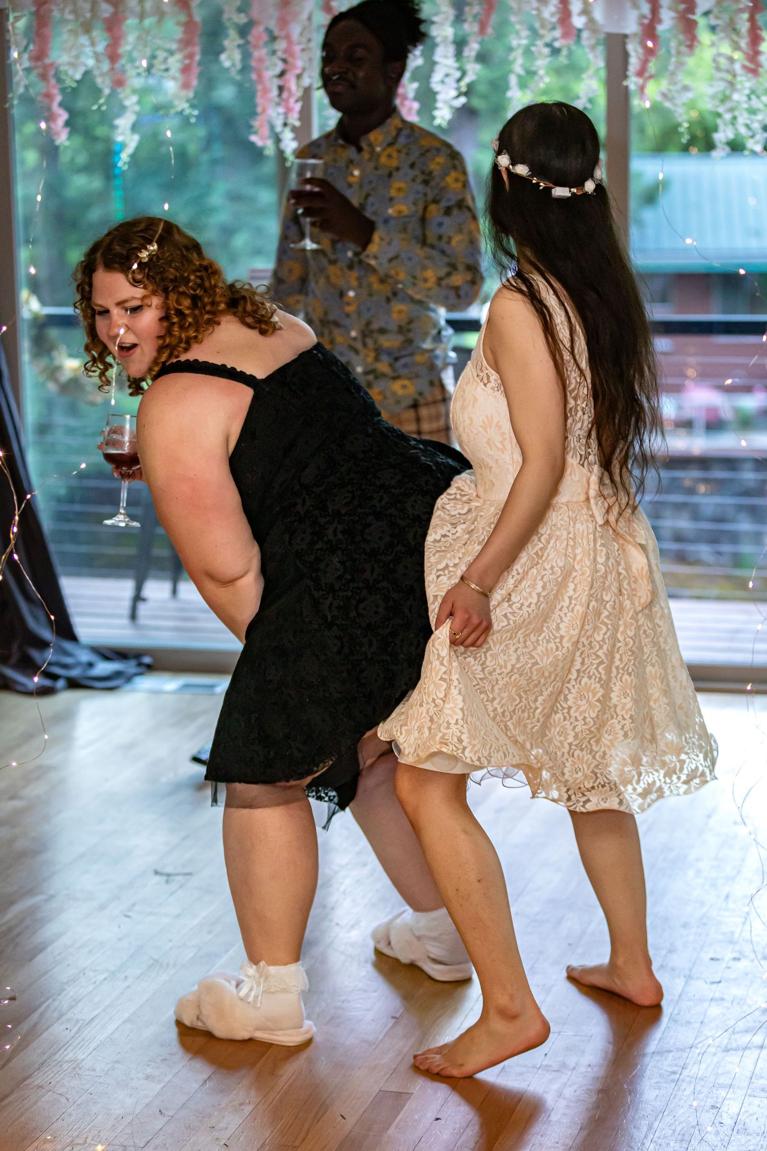 Wedding guests dancing barefoot on a wooden floor under decorative hanging lights.