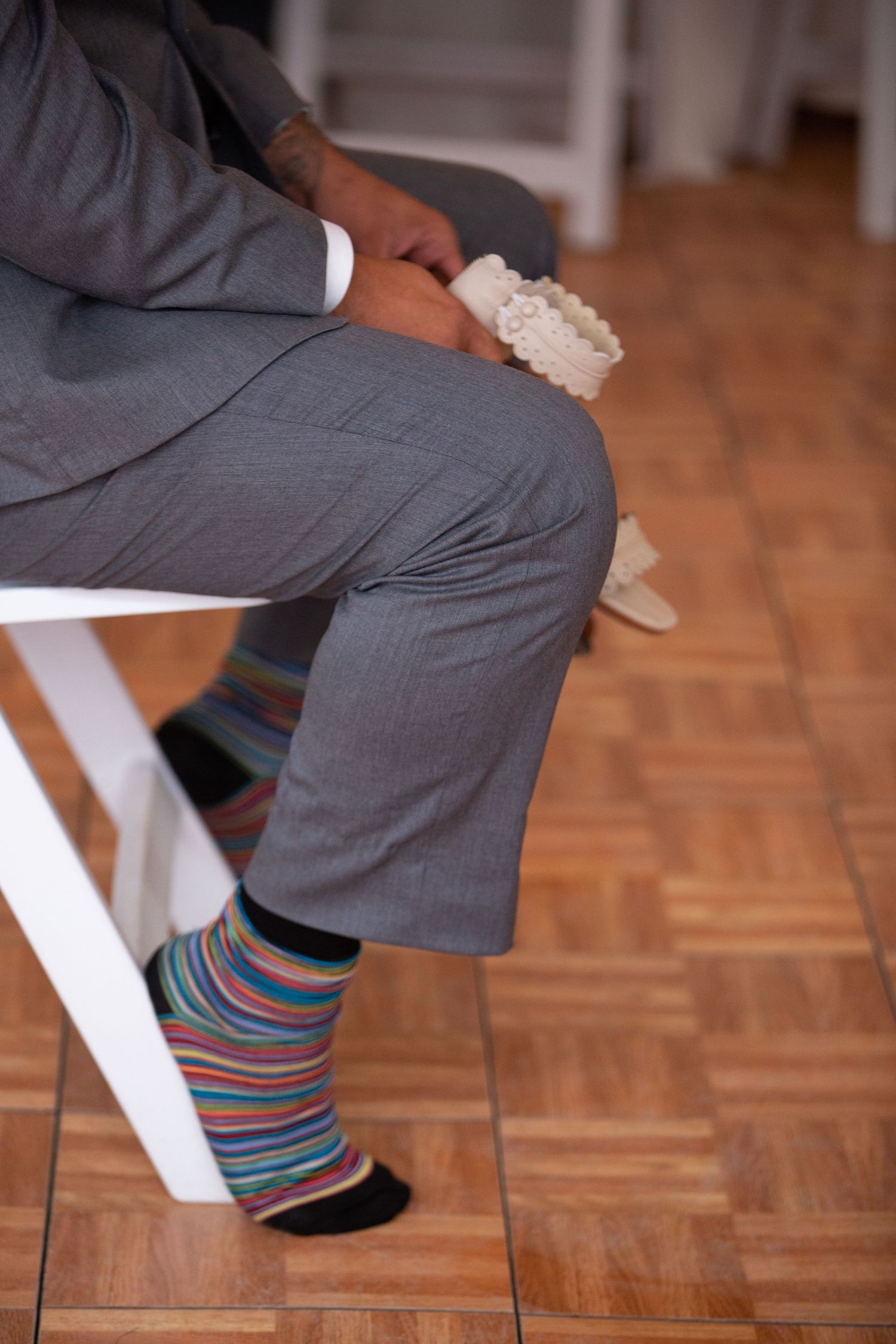 Close-up of a person in a gray suit showing colorful striped socks while seated on a white chair.