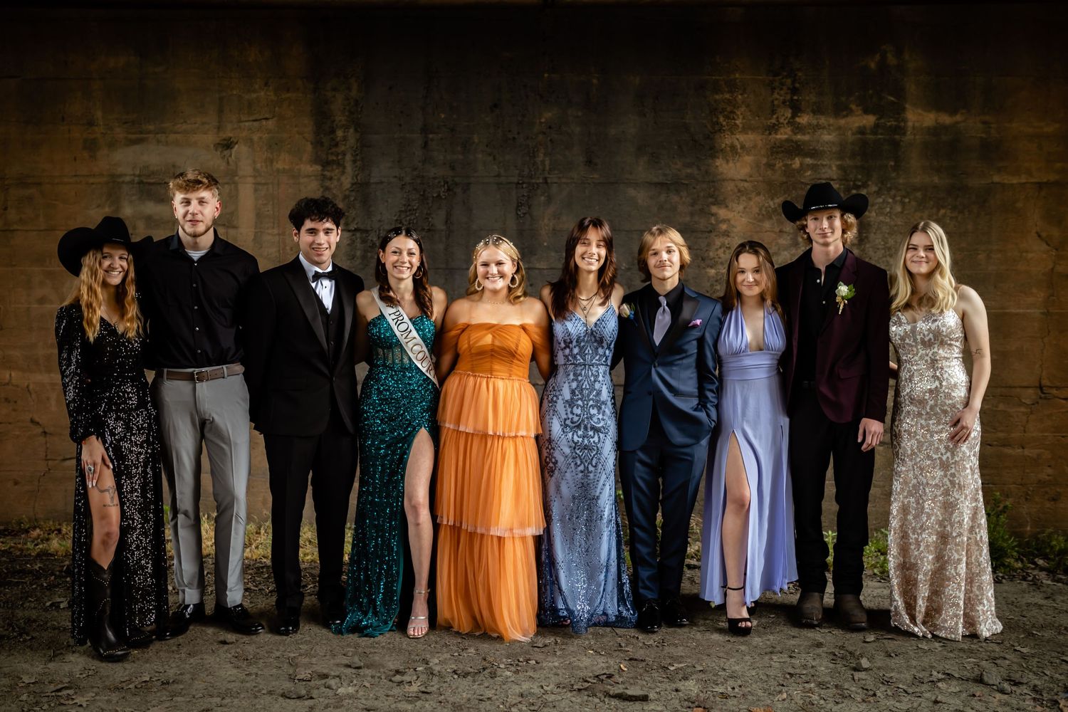 A group photo of formally dressed people standing against a rustic brick wall.