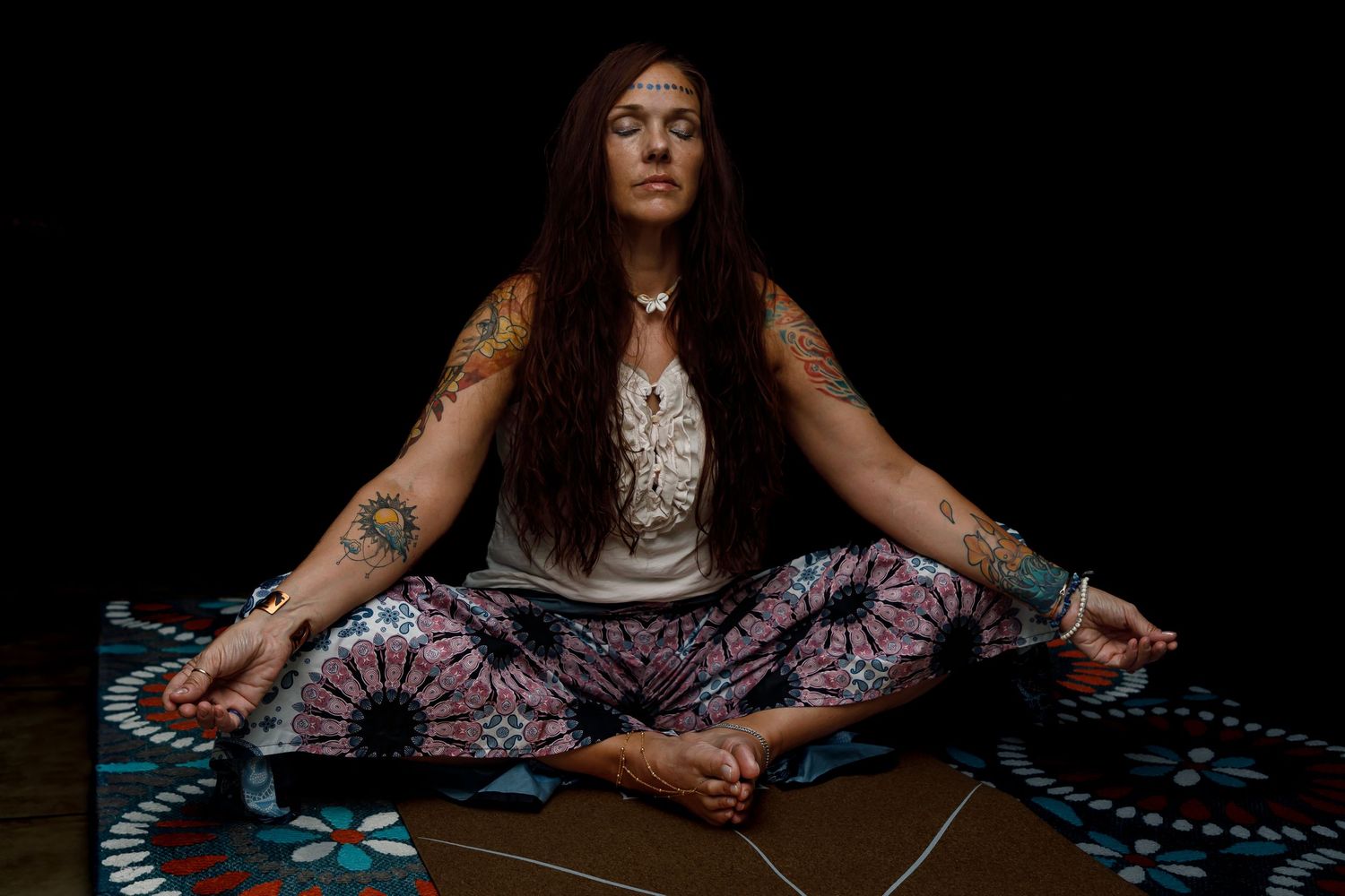 Meditative pose on patterned floor in dark atmospheric lighting.