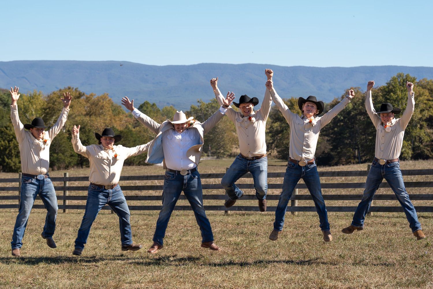 Wedding party jumps in unison against mountain backdrop during sunset photo session.