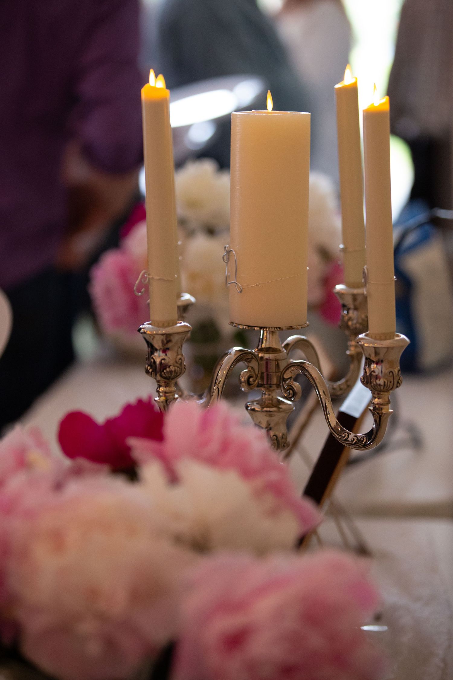 Elegant candelabras with lit white candles surrounded by pink floral arrangements on dining tables at a wedding reception.
