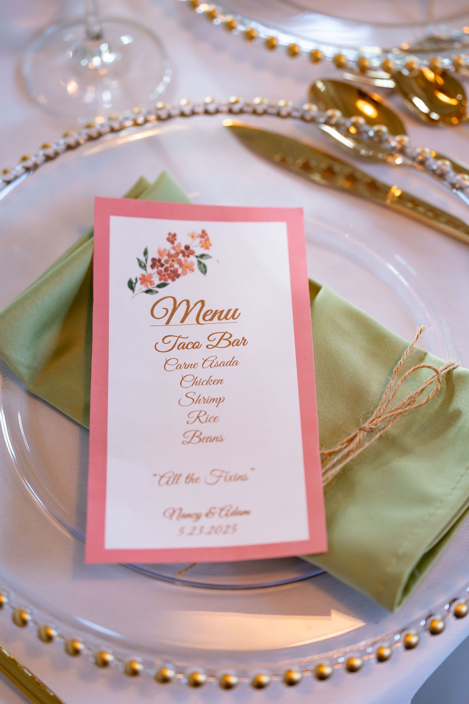 Pink menu card with floral design placed on mint napkin atop decorative gold-rimmed plate.