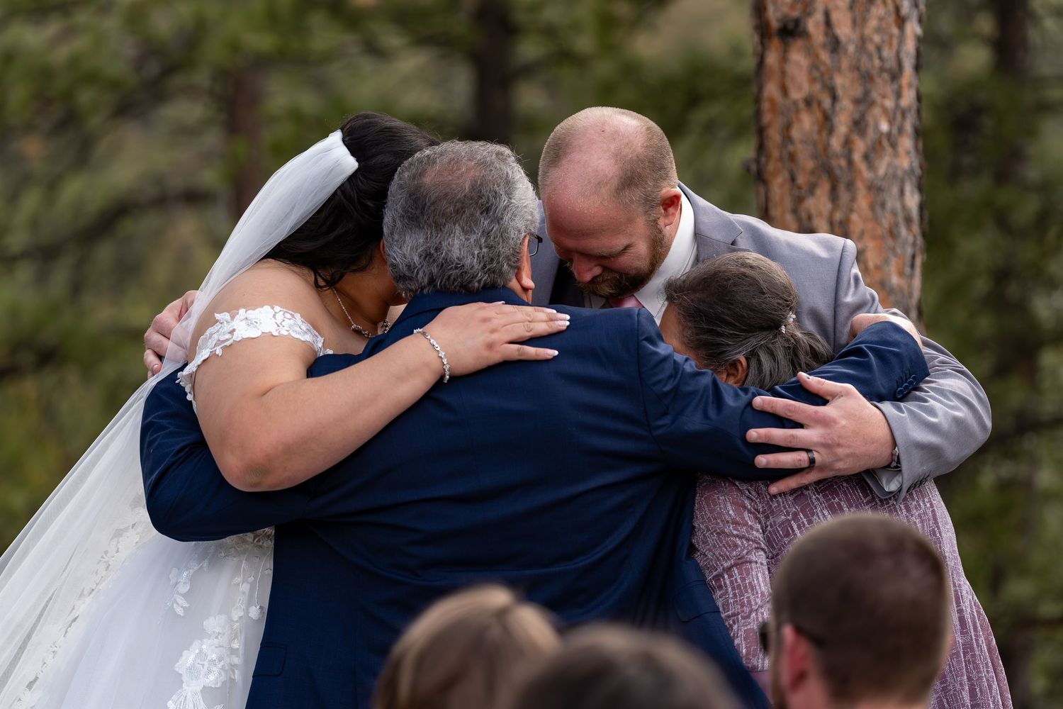 Emotional outdoor wedding ceremony with heartfelt embraces between loved ones under pine trees.