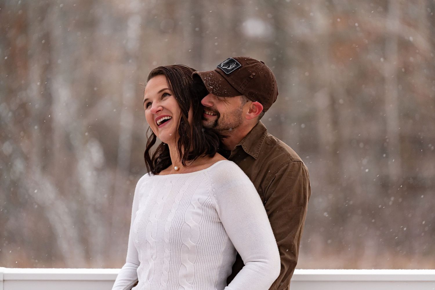 Snowy engagement session captures couple's laughter in winter setting.