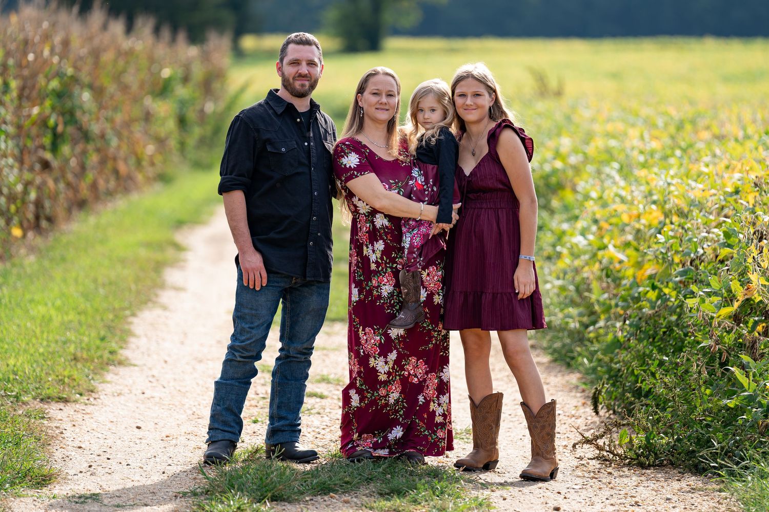 Family portrait session in a sunny field with wildflowers and natural outdoor setting.