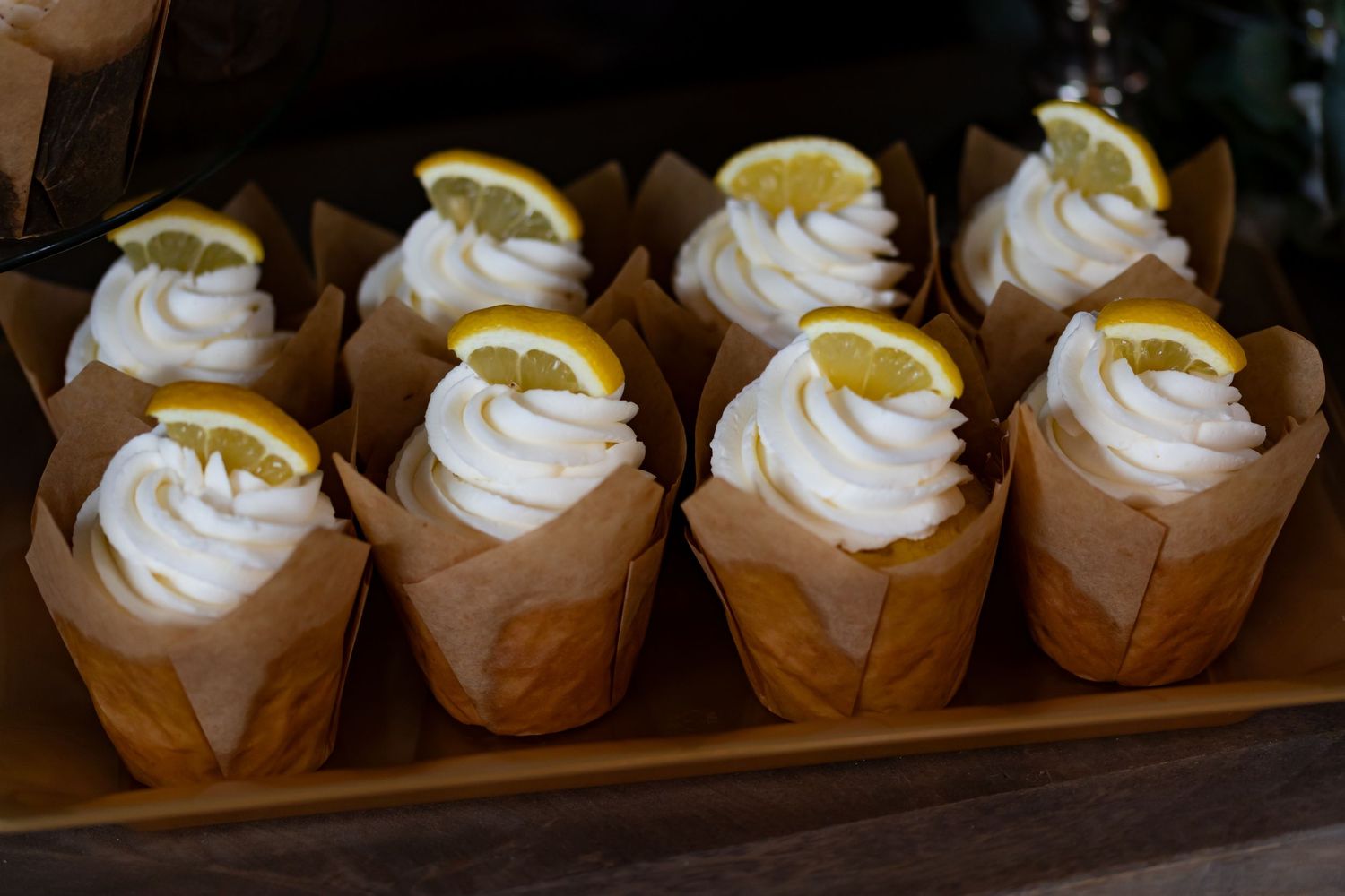 Lemon garnished cupcakes with white frosting displayed in brown paper liners.