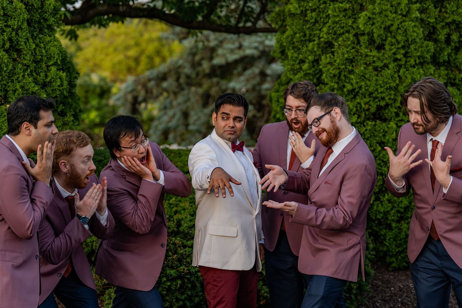 Groomsmen in matching mauve suits share a candid moment during a wedding celebration.