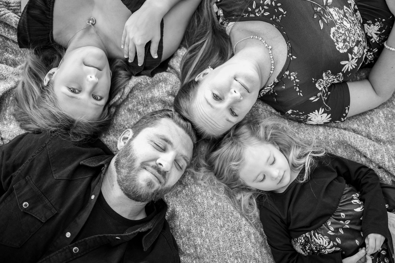 Overhead black and white portrait of family lying in circle on carpet.