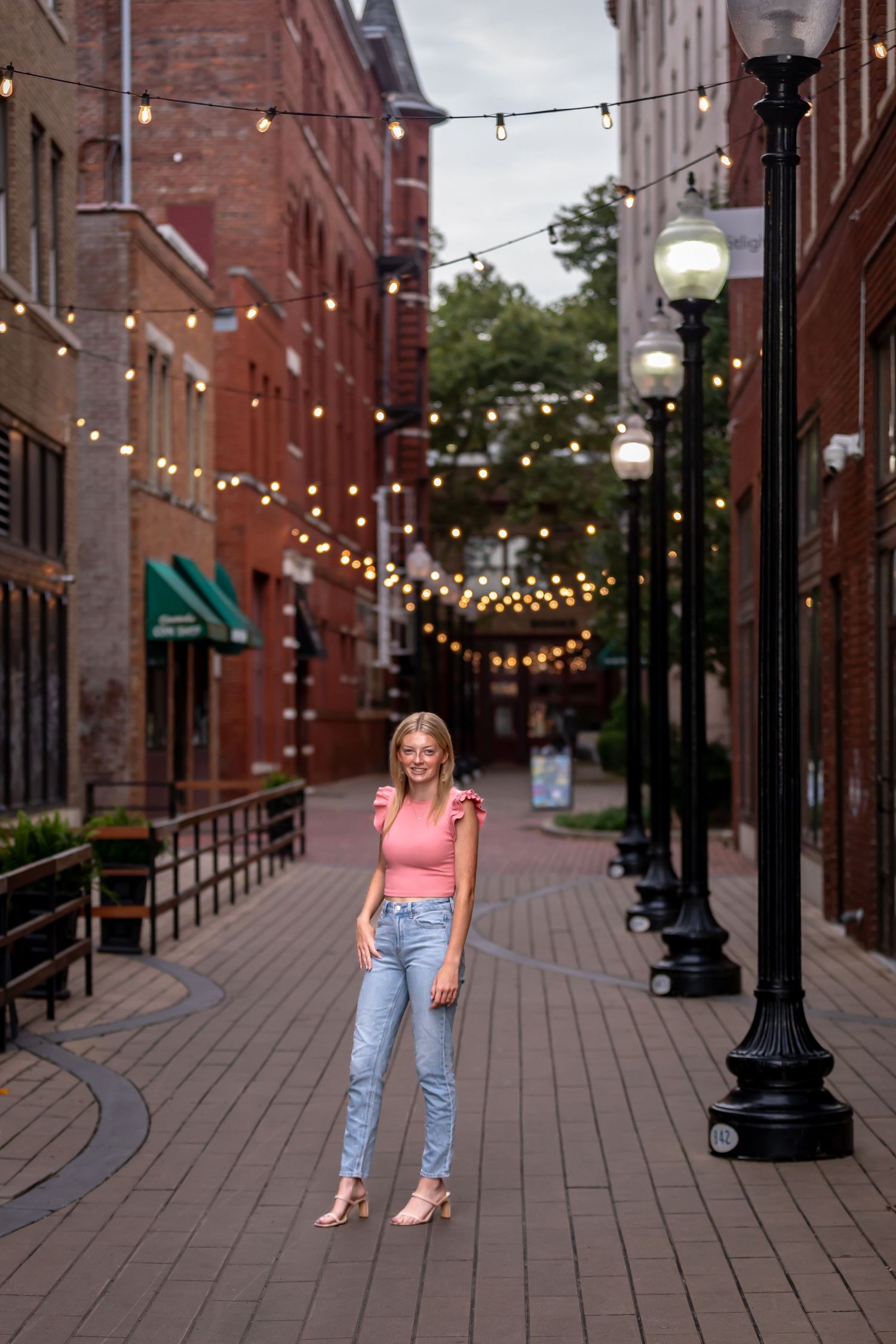 String lights illuminate brick alley during evening urban photoshoot.