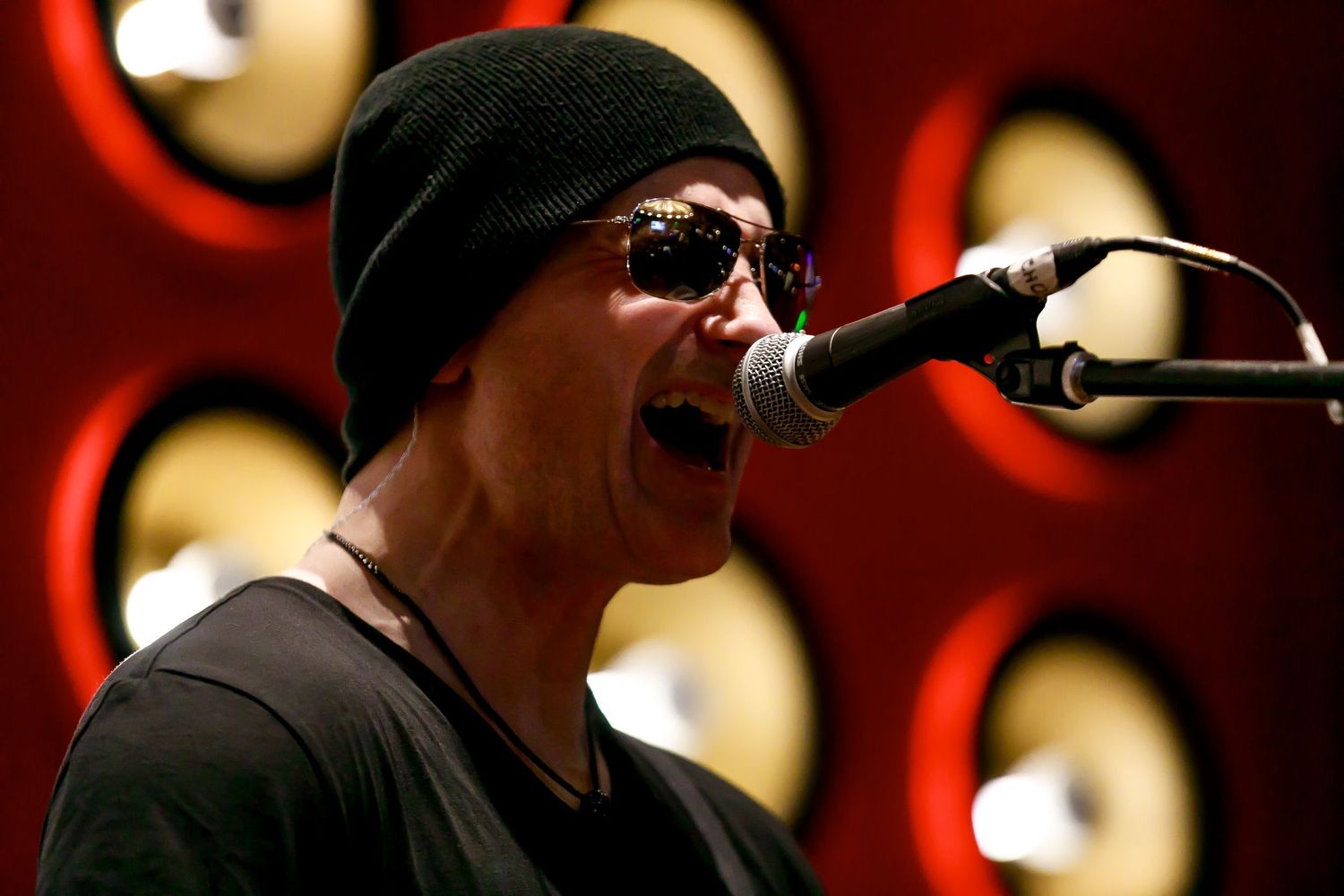 Close-up of performer singing into microphone in red-lit venue.