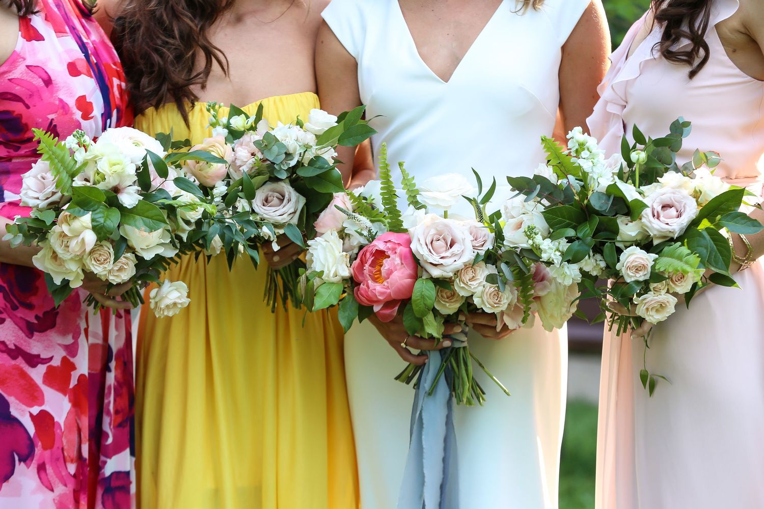 Bridesmaids in bright yellow dresses hold elegant pink and white floral bouquets against a green background.