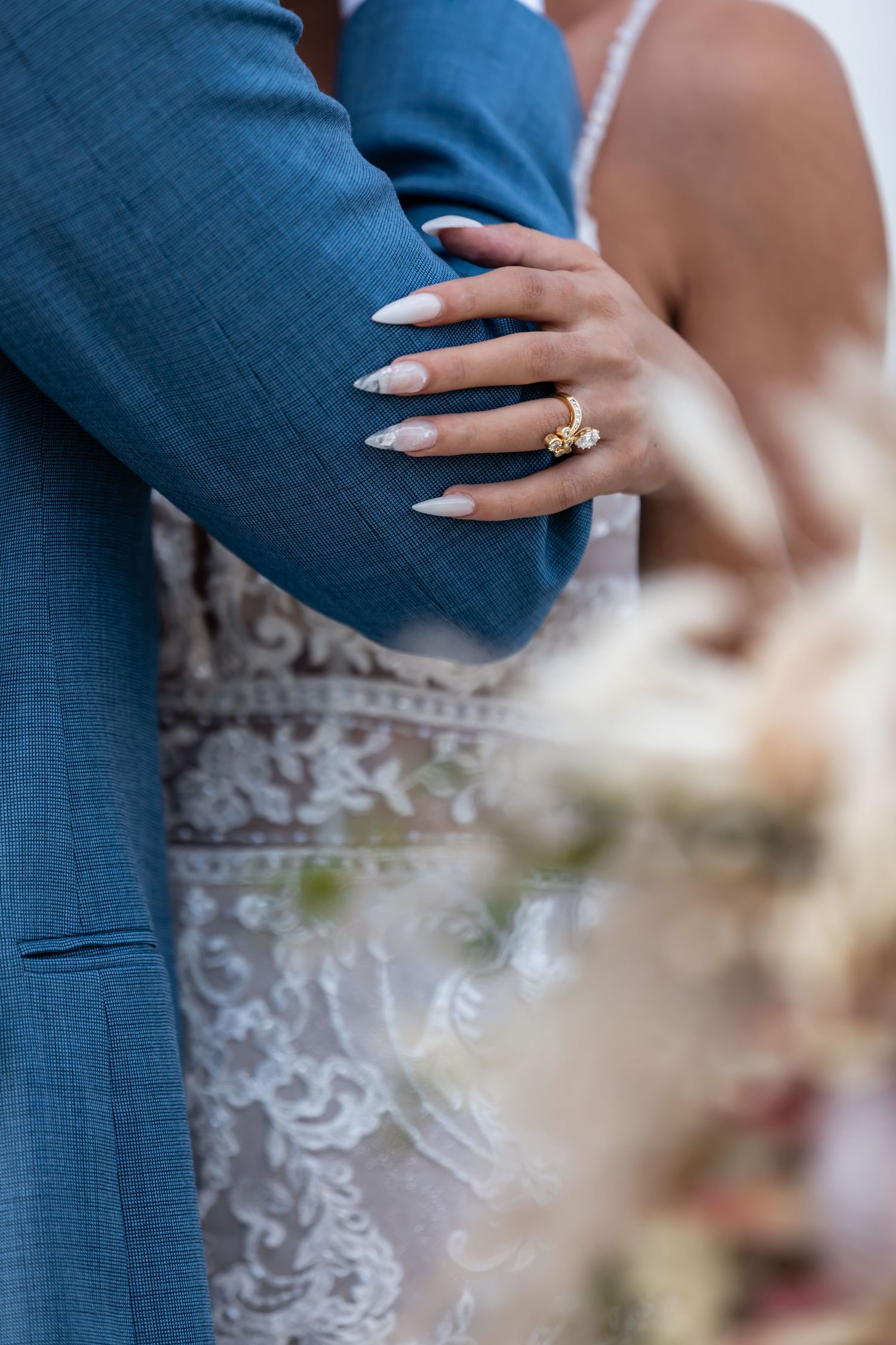 Close-up of a hand with long white nails and engagement ring resting on a navy blue suit jacket.