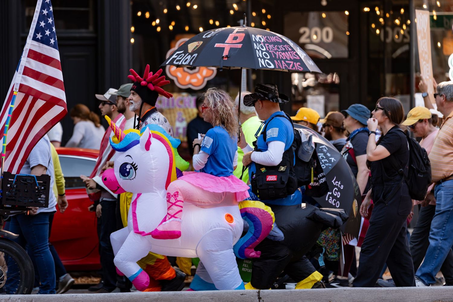 Crowd at protest with inflatable unicorn float and American flag.