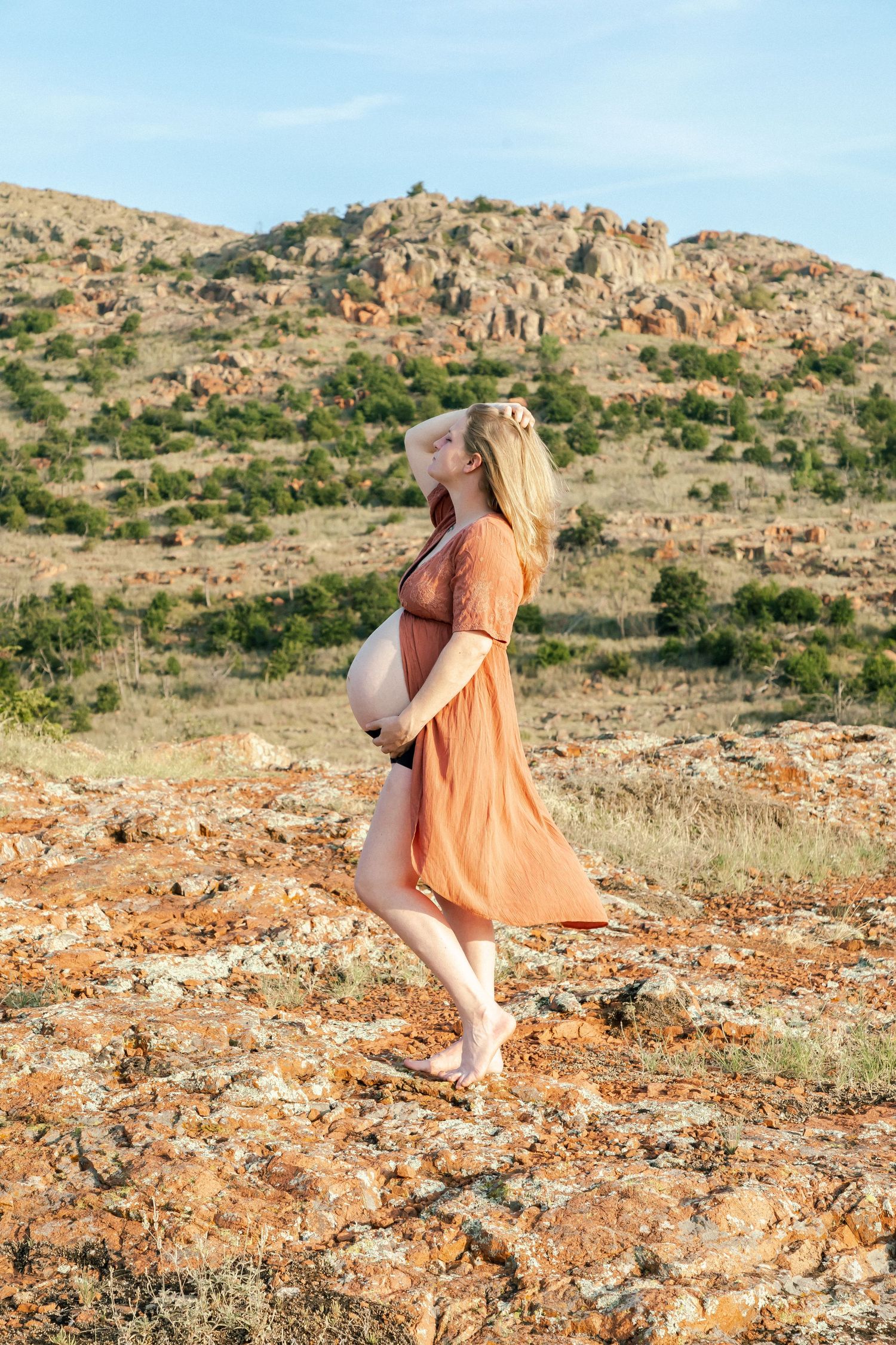 Figure in peach dress poses gracefully on rocky terrain with mountains in background.