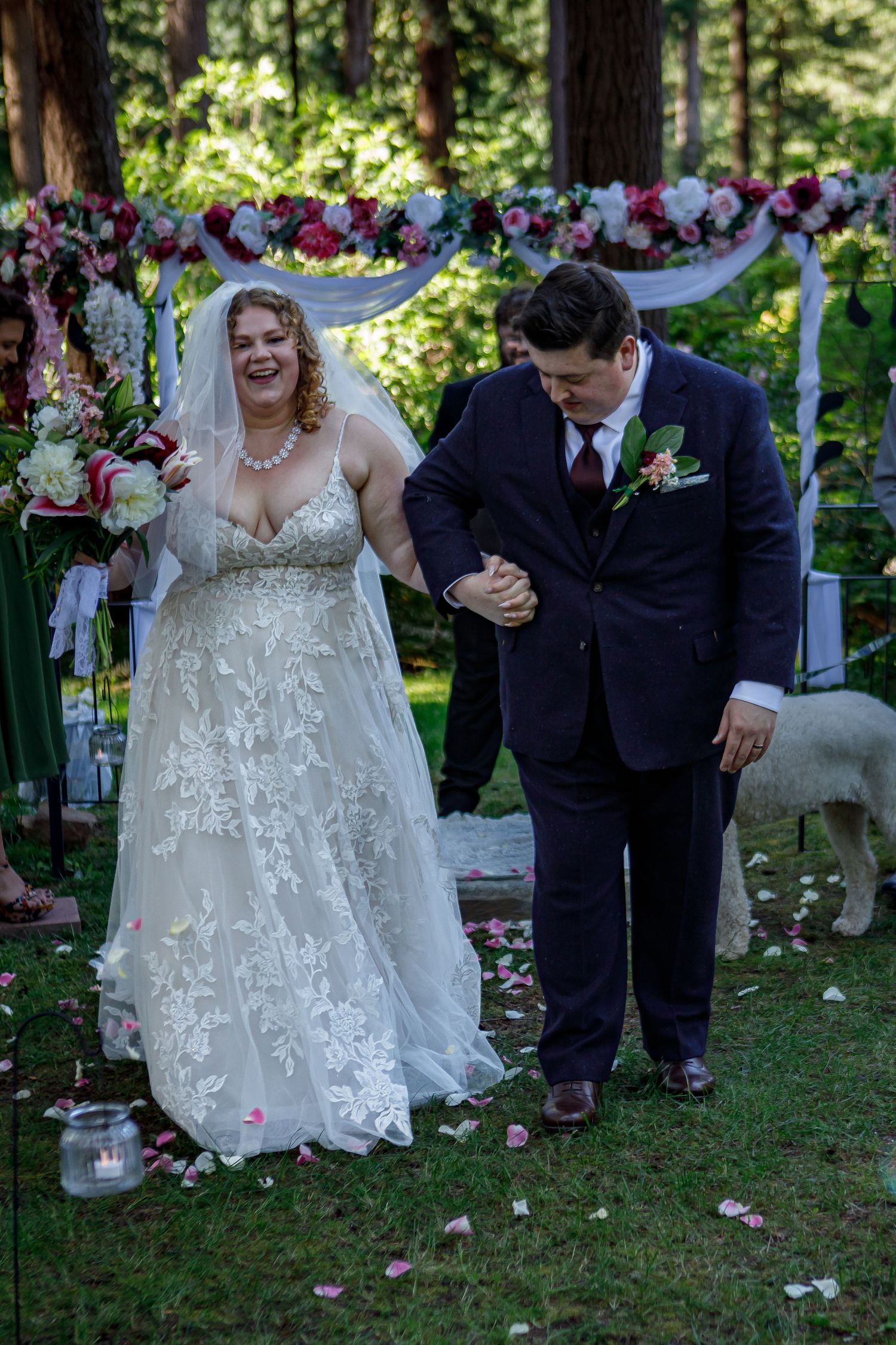 Joyful wedding celebration with flower petals being tossed in wooded outdoor setting.
