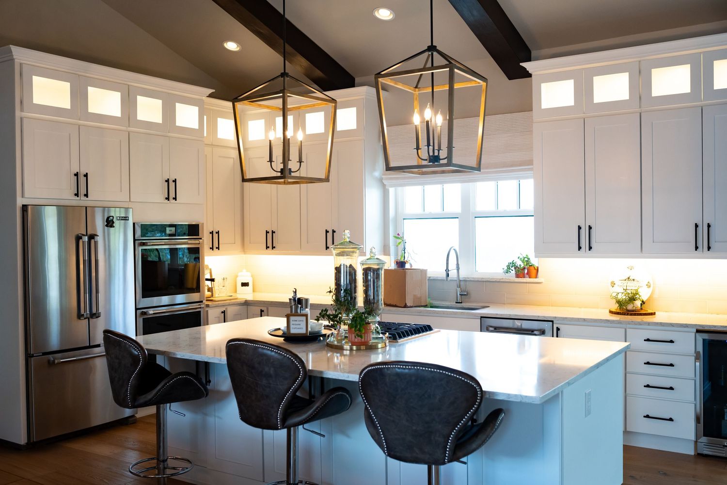 Modern white kitchen with rustic wood beams and pendant lighting.