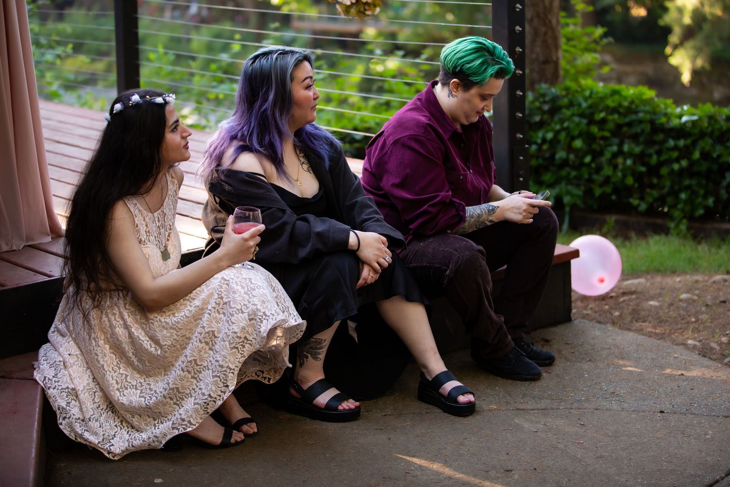 Wedding guests relax on benches in a garden setting during an outdoor reception.