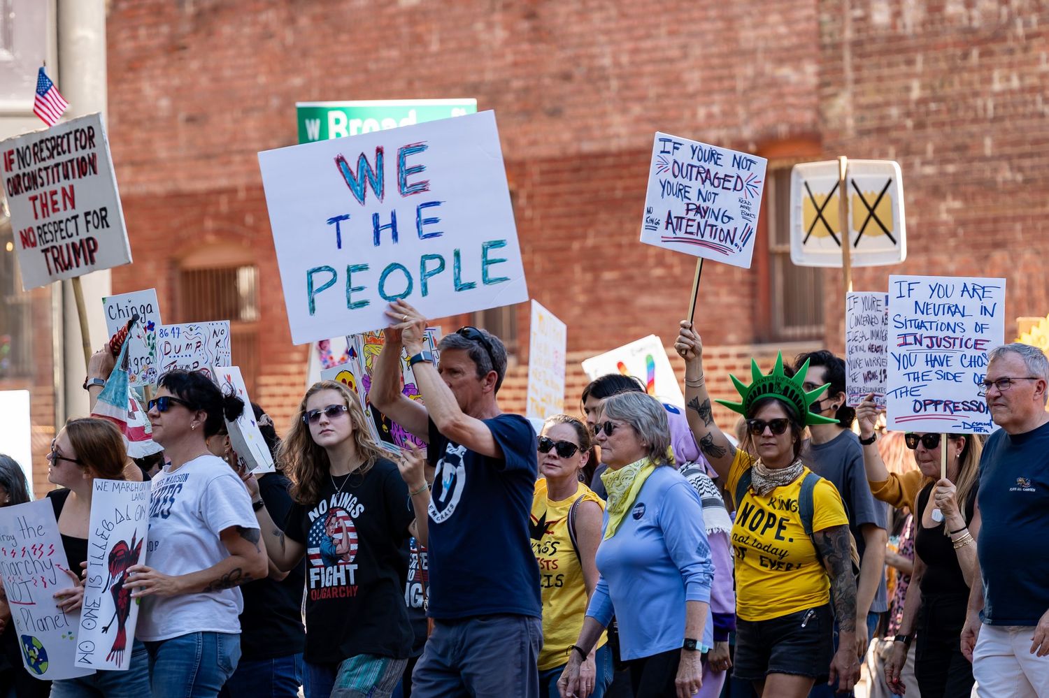 Protesters holding various signs including 'We The People' during street demonstration.