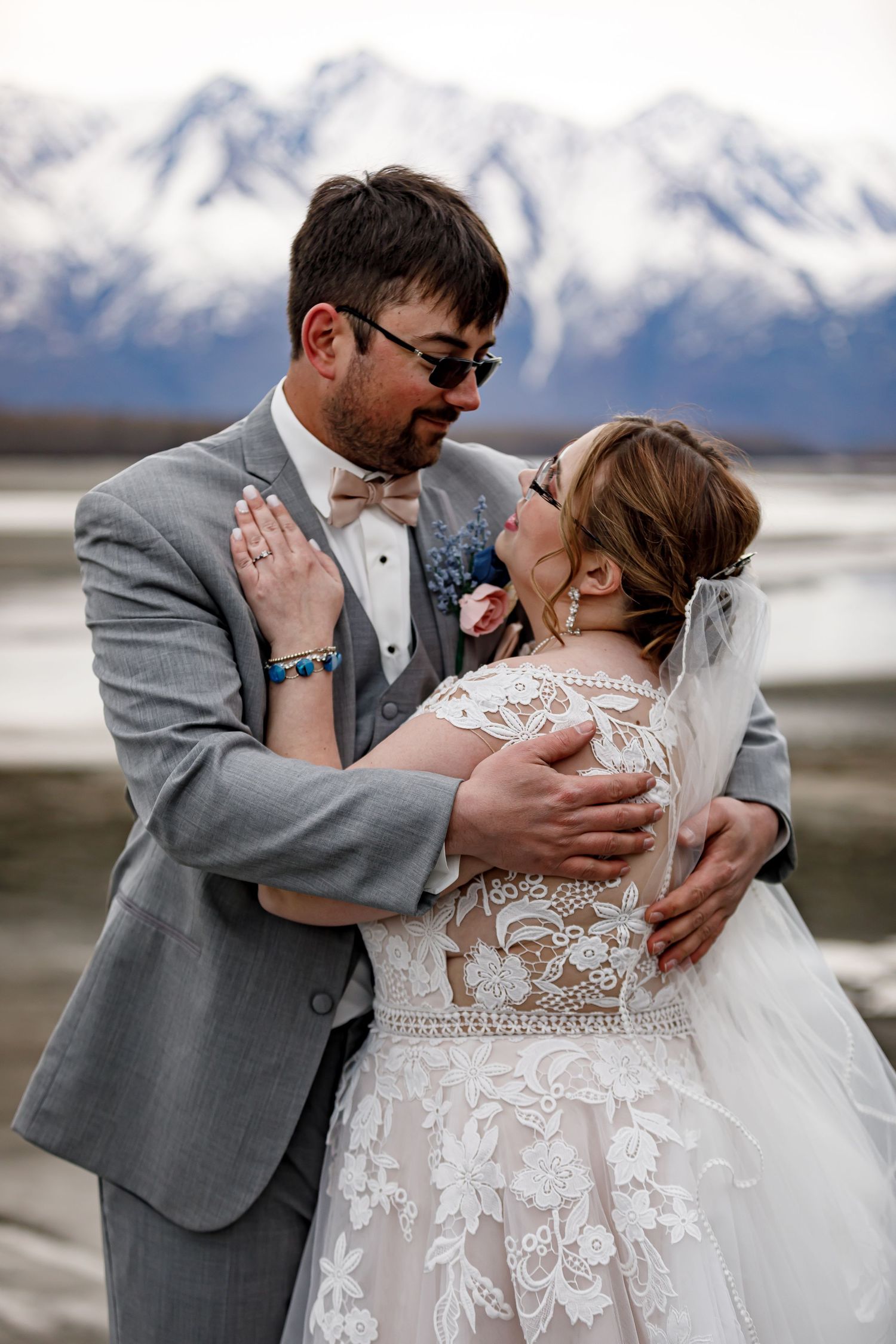 Wedding couple embracing with snow-capped mountains in background.
