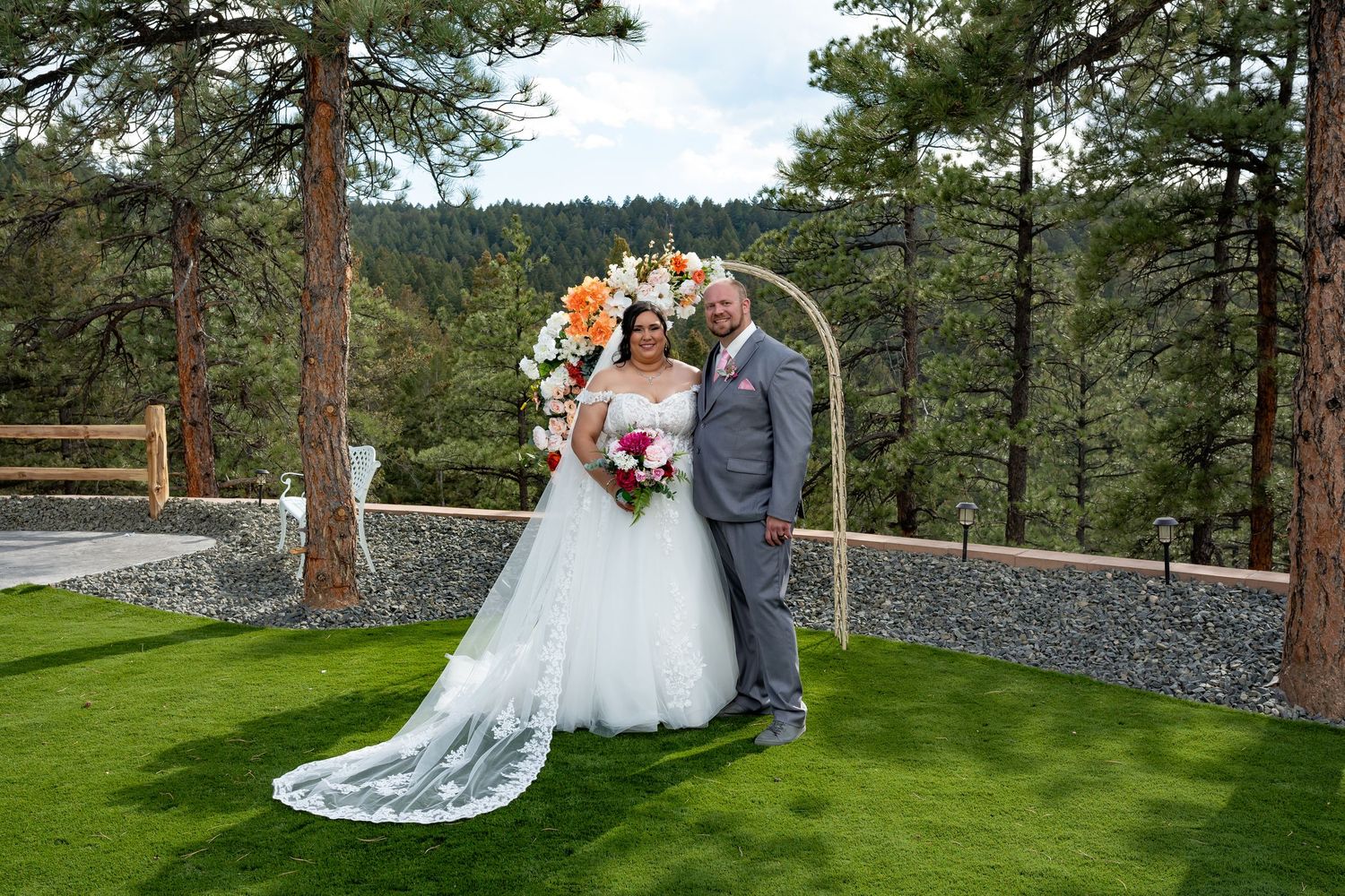 Wedding ceremony setup in a scenic mountain location with pine trees and stone wall.