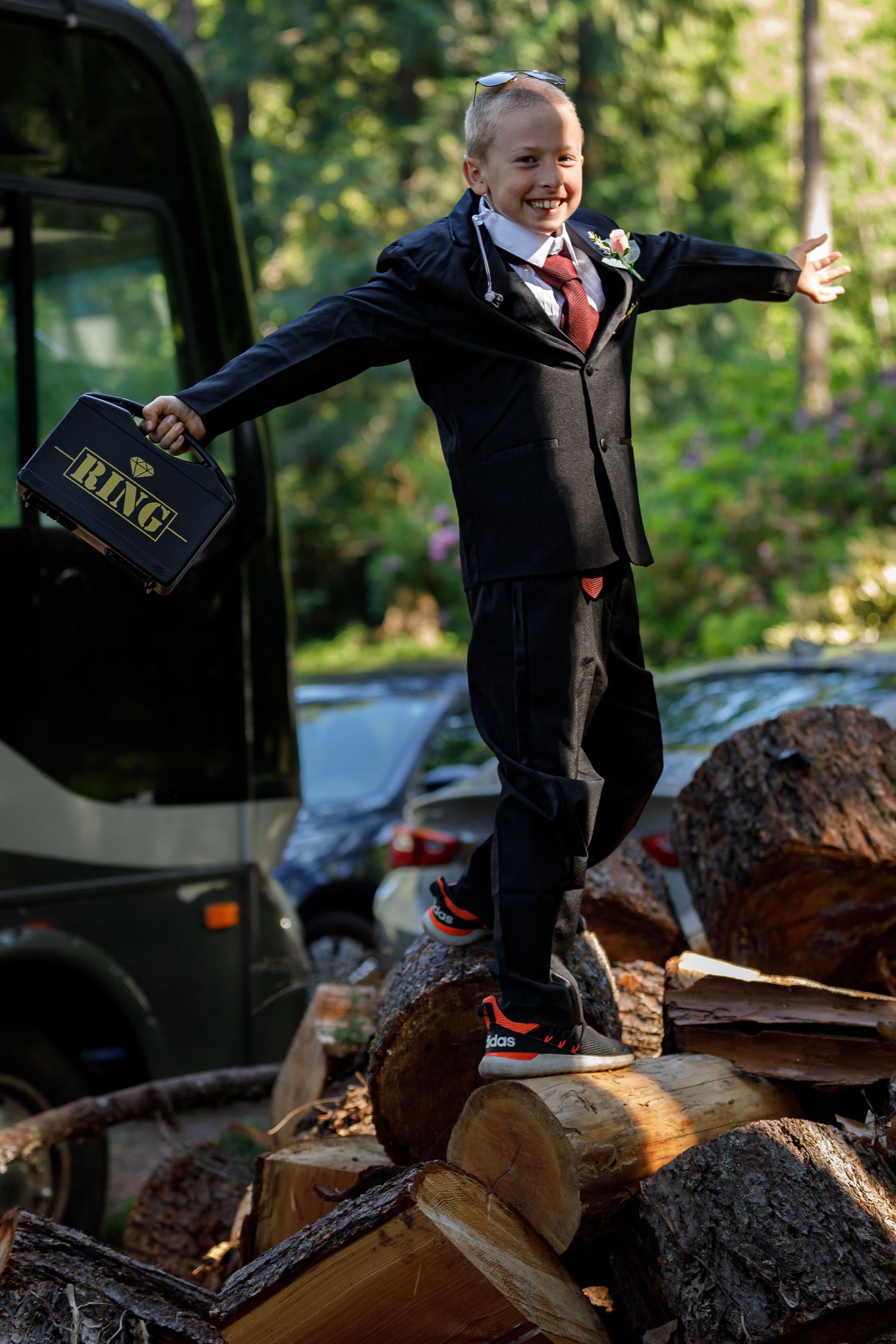 Person in formal attire standing on woodpile during outdoor photoshoot.