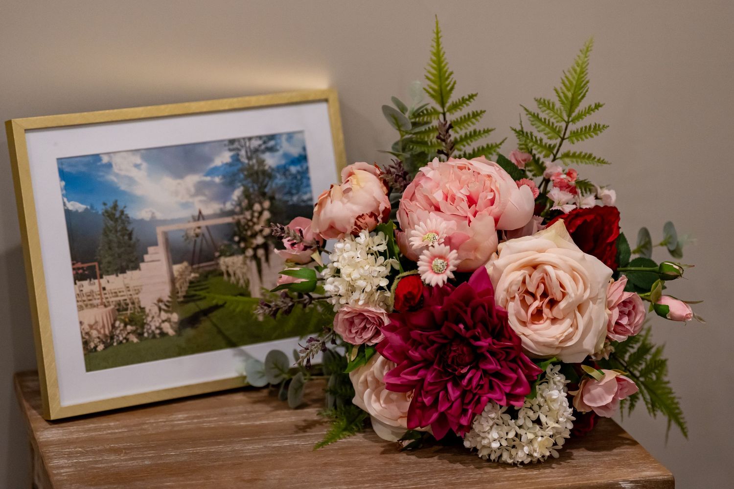 Pink and burgundy floral arrangements with ferns displayed next to framed photographs.
