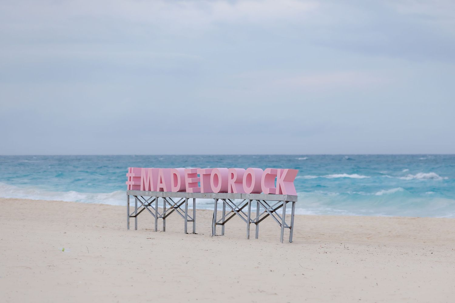 Panoramic view of empty beach with Made By Rock text installation on shoreline.