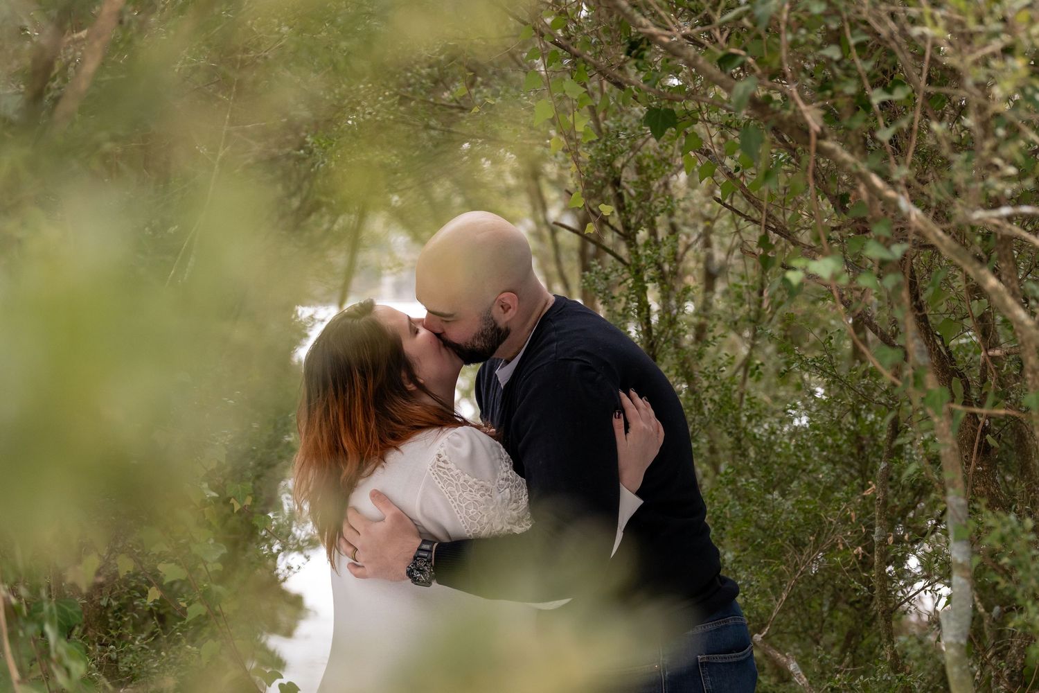 Romantic couple embraces among green foliage in a garden setting.