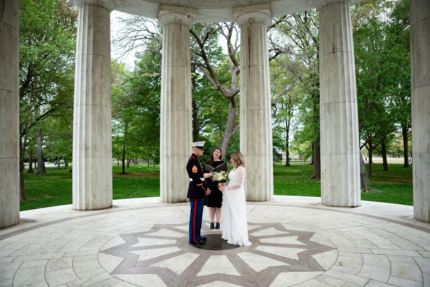 Wedding couple photographed in circular marble monument surrounded by columns and greenery.