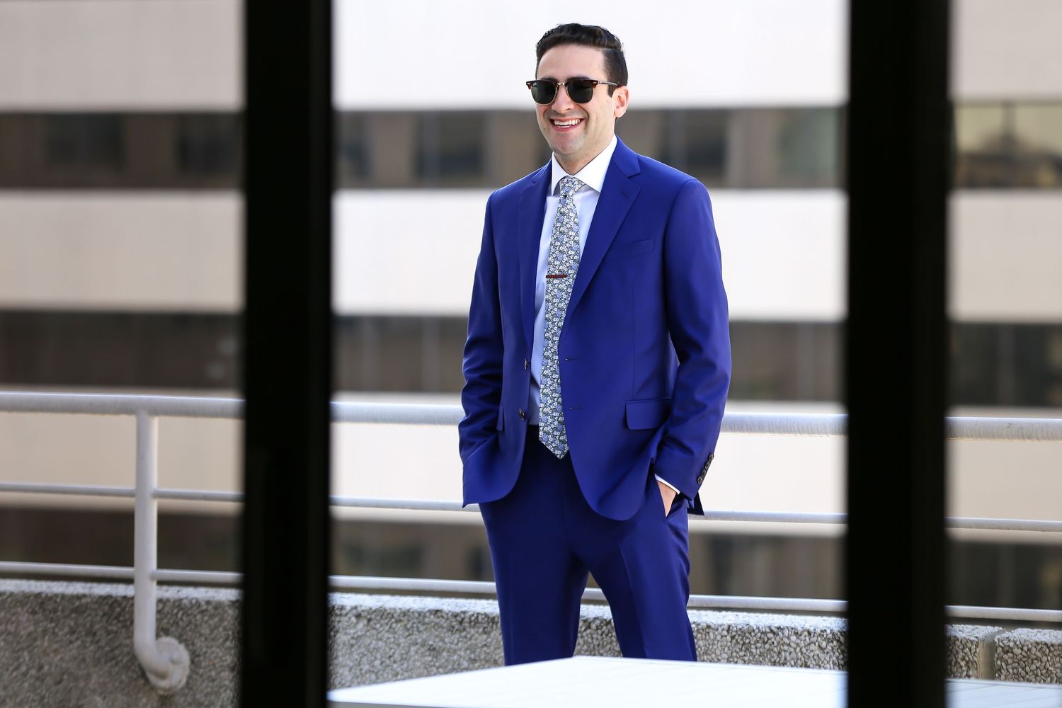 Groom in navy blue suit poses against white architectural background.