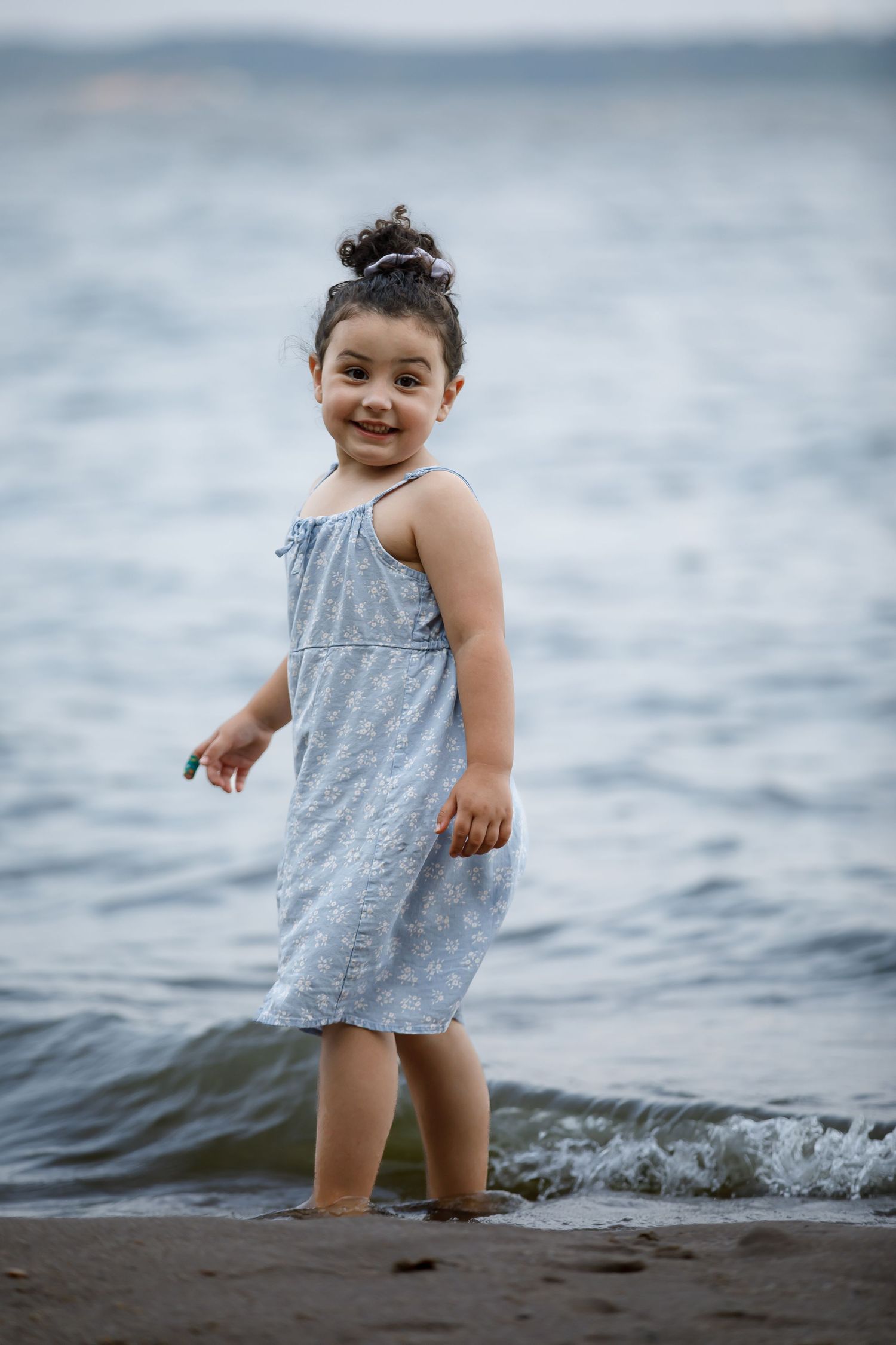 Young child in a gray dress plays joyfully in the ocean waves.